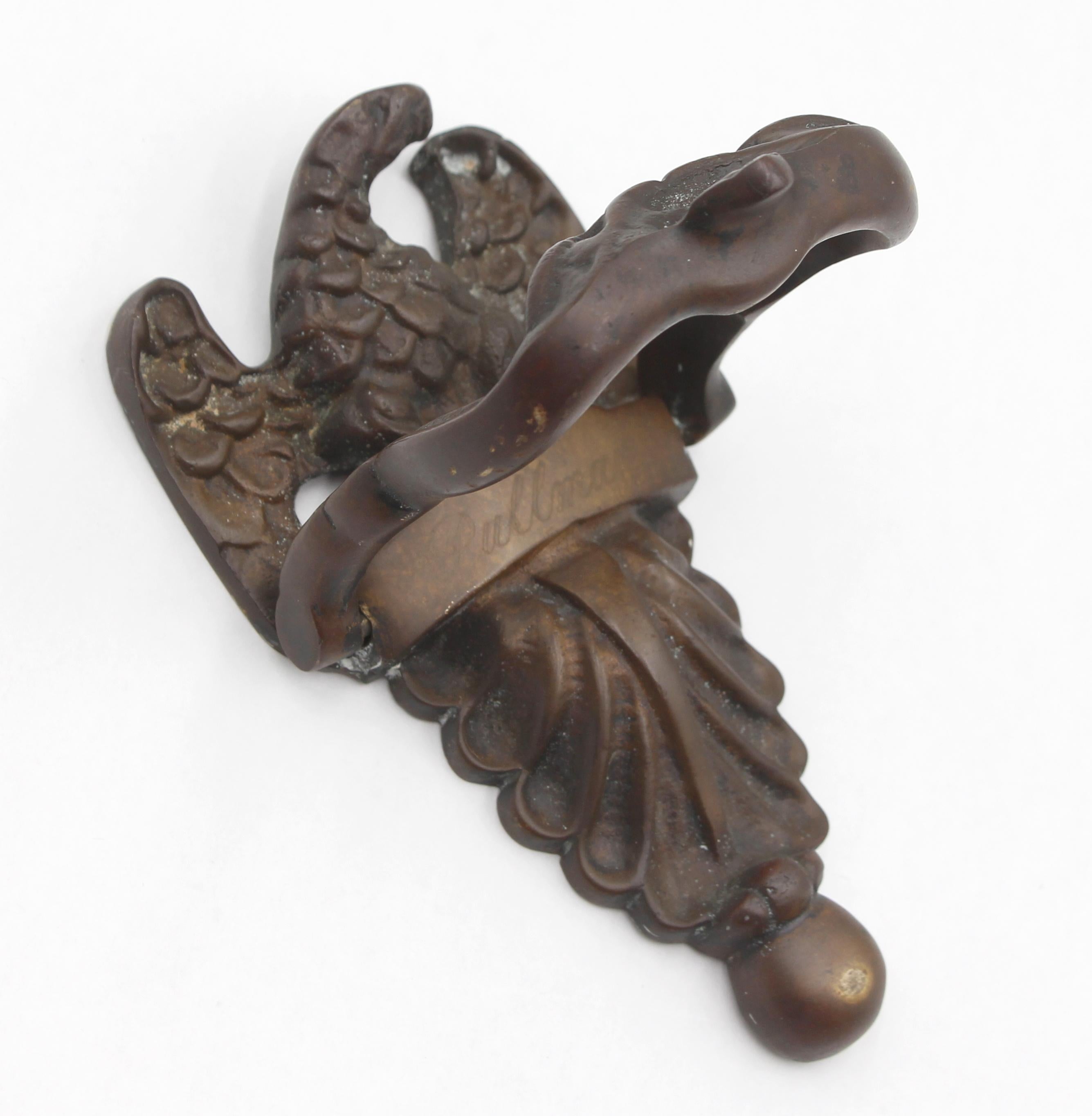 Bronze door knocker featuring an eagle with outstretched wings perched above a decorative banner and a leaflike design. Inscribed Pullman. Mounting screws are included. Good condition with surface wear from prior use. One available. Please note,