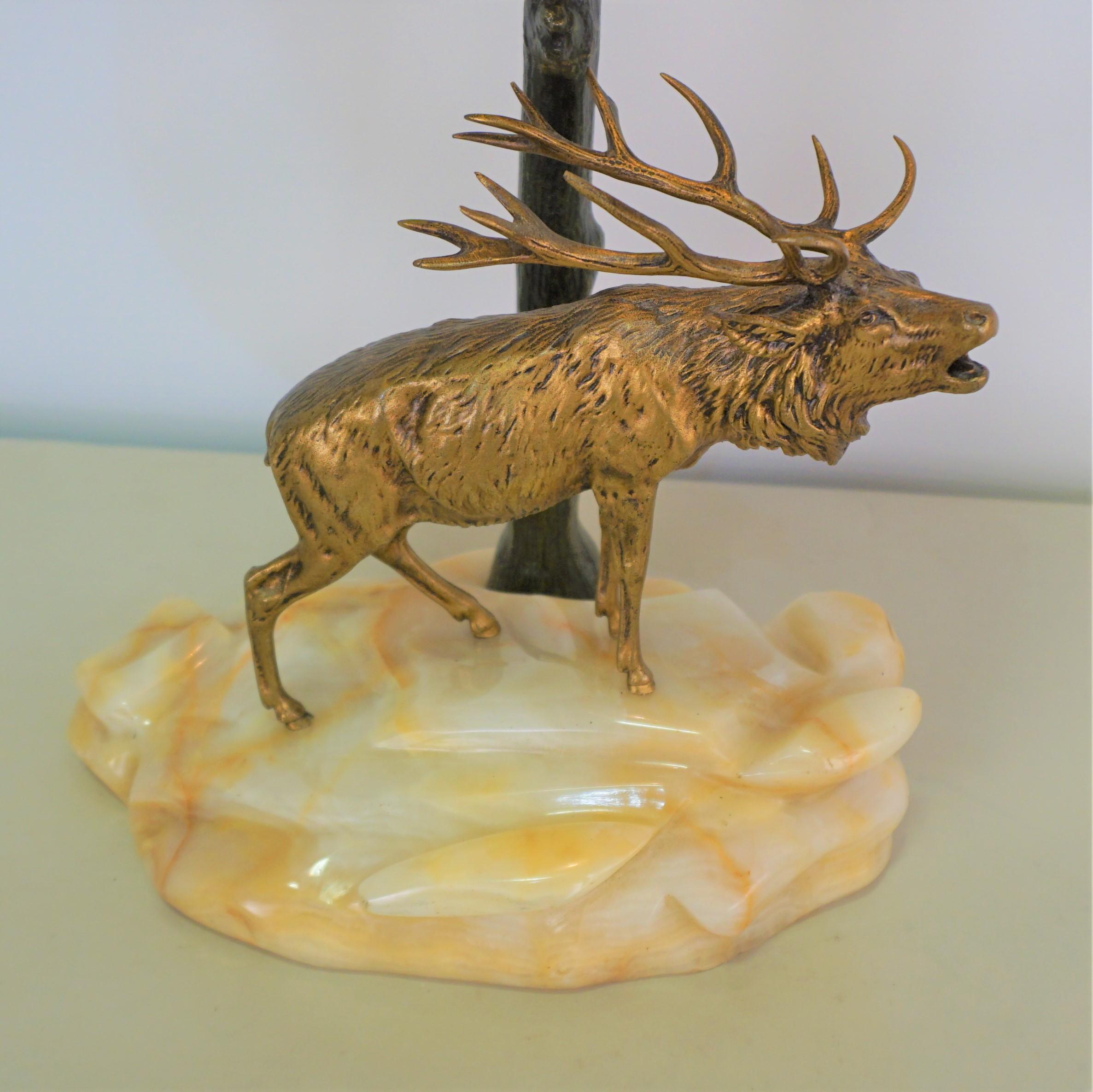 A fabulous desk lamp with golden bronze buck standing on piece of rock, dark green-black tree trunk as base that art glass shade rest on.
