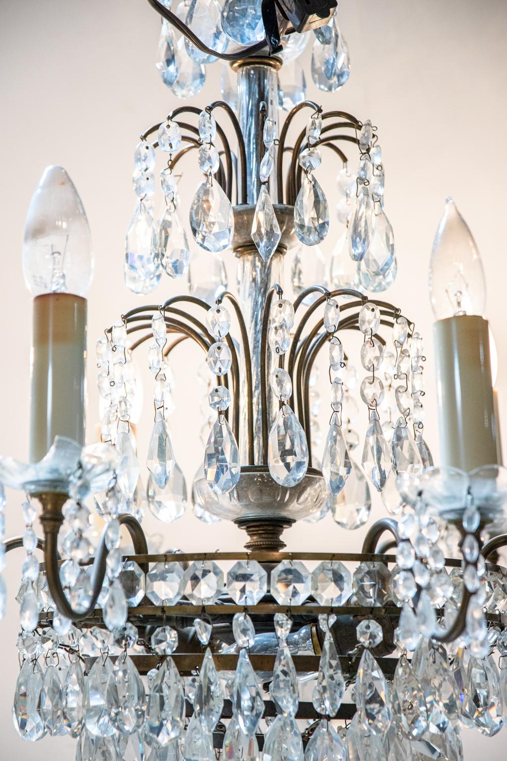 Bronze and cut crystal chandelier with four tiers of almond pendant crystal prisms. The piece features further almond shaped prisms hanging underneath the scalloped trim bobeches. Please note of wear consistent with age including patina to the