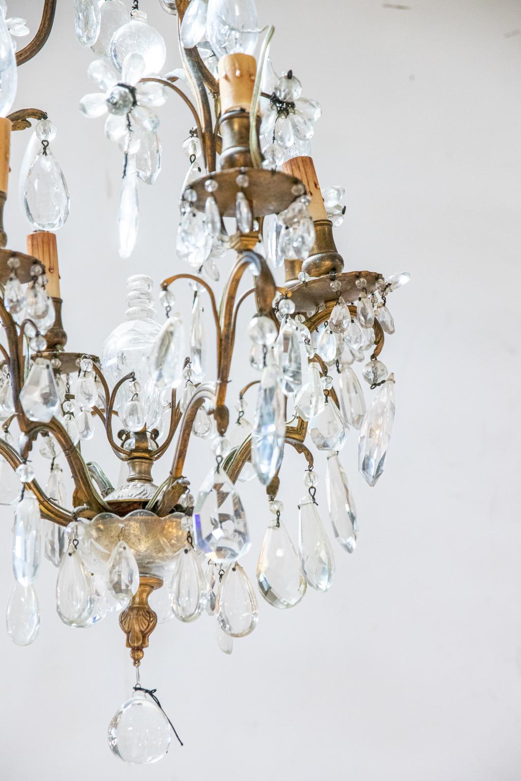 French bronze chandelier with six arms and various pendant almond shaped prisms. These prisms can be seen underneath the arms and bobeches. The chandelier is also constructed with a large glass bulb finial at the center of the piece. Please note of