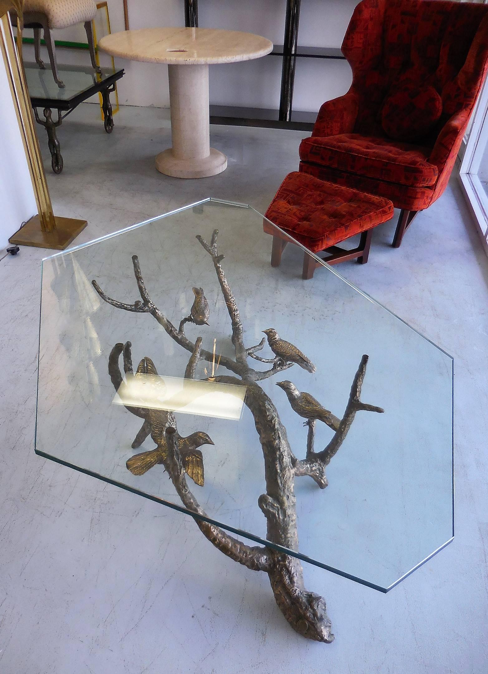 Solid bronze coffee table with asymmetric glass top. An almost surreal depiction of birds perched on a large branch becomes the base for this table.