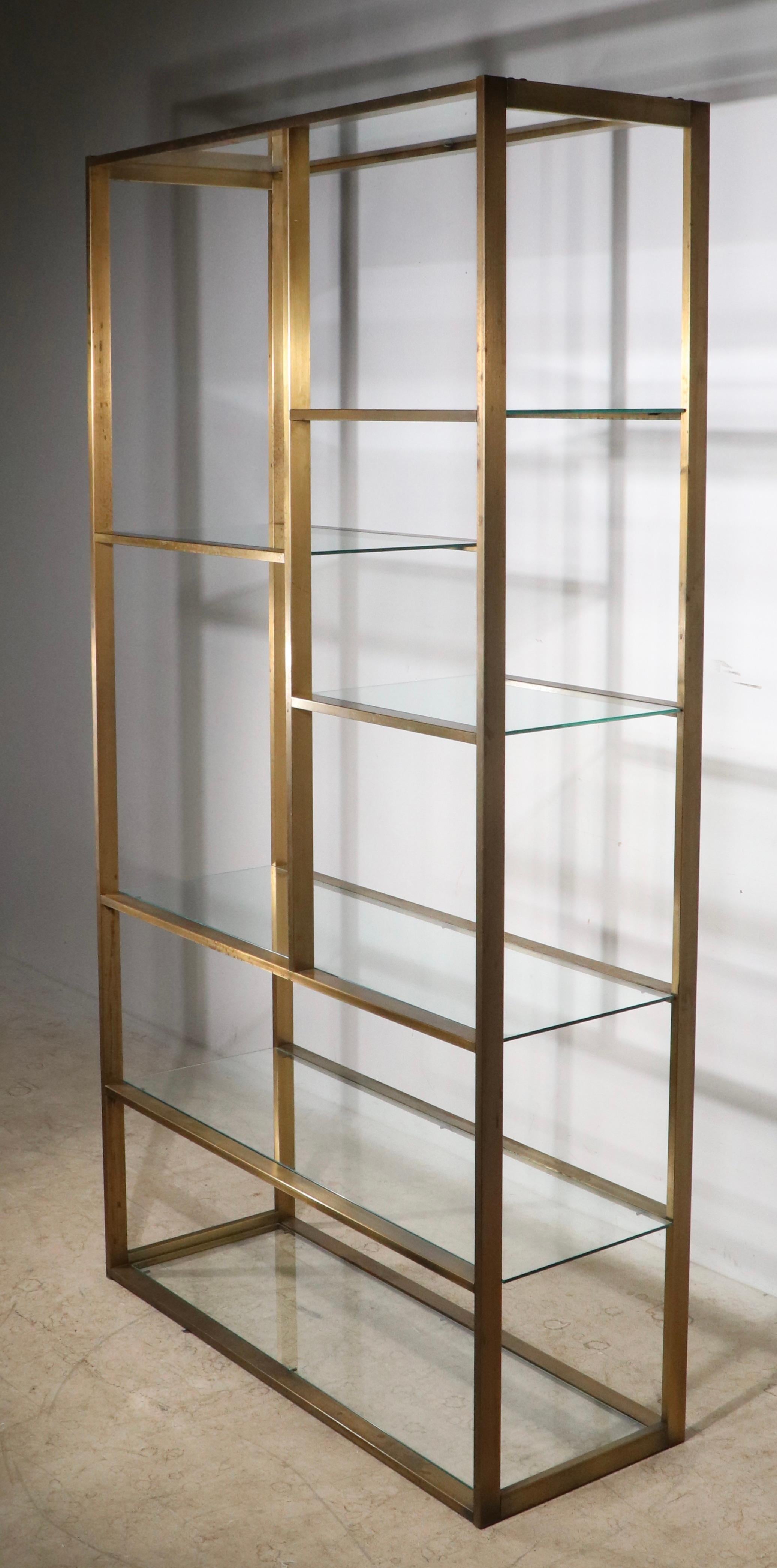 Architectural, voguish, stylish freestanding shelf unit, design attributed to Milo Baughman.  This model is particularly chic in the brass, bronze finish, it is more commonly found in chrome. The metal frame is in good, original condition, it shows