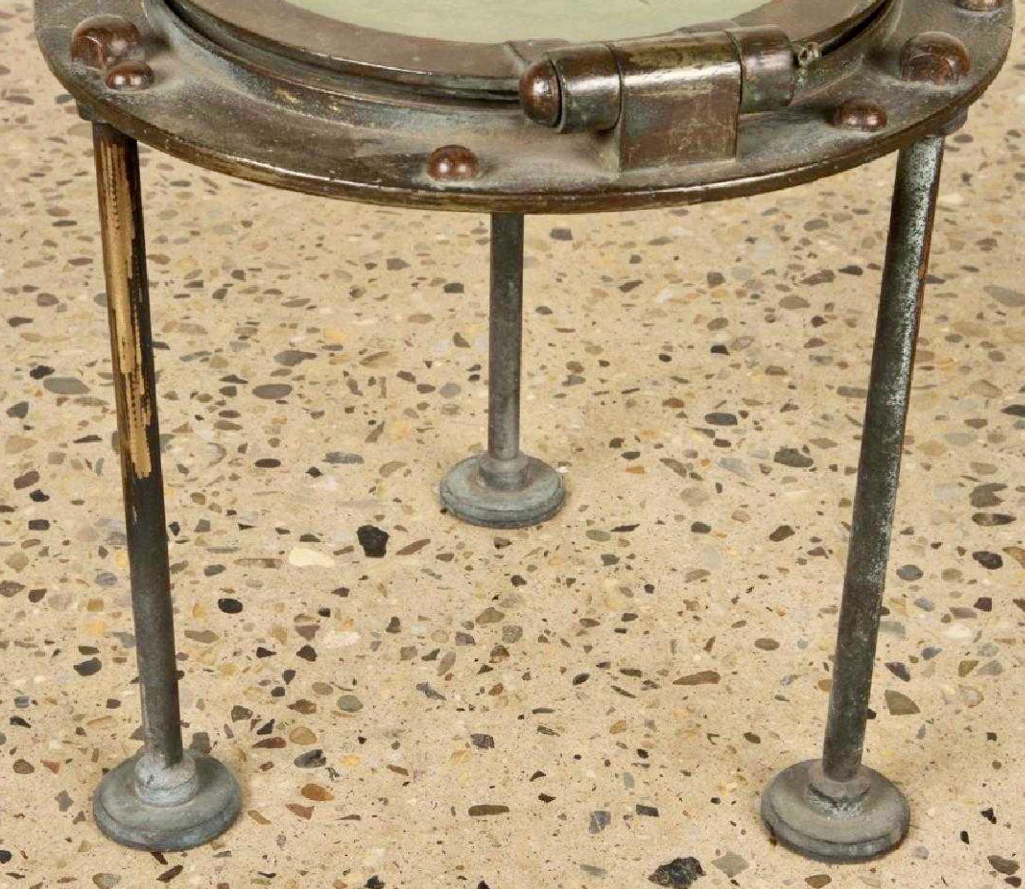 Interesting side table made from an old ship's porthole. Tripod legs. Bronze porthole with iron legs and brass hardware. Exceptionally well done. Original glass has patina with a frosted appearance. Great conversation piece. Good vintage condition.