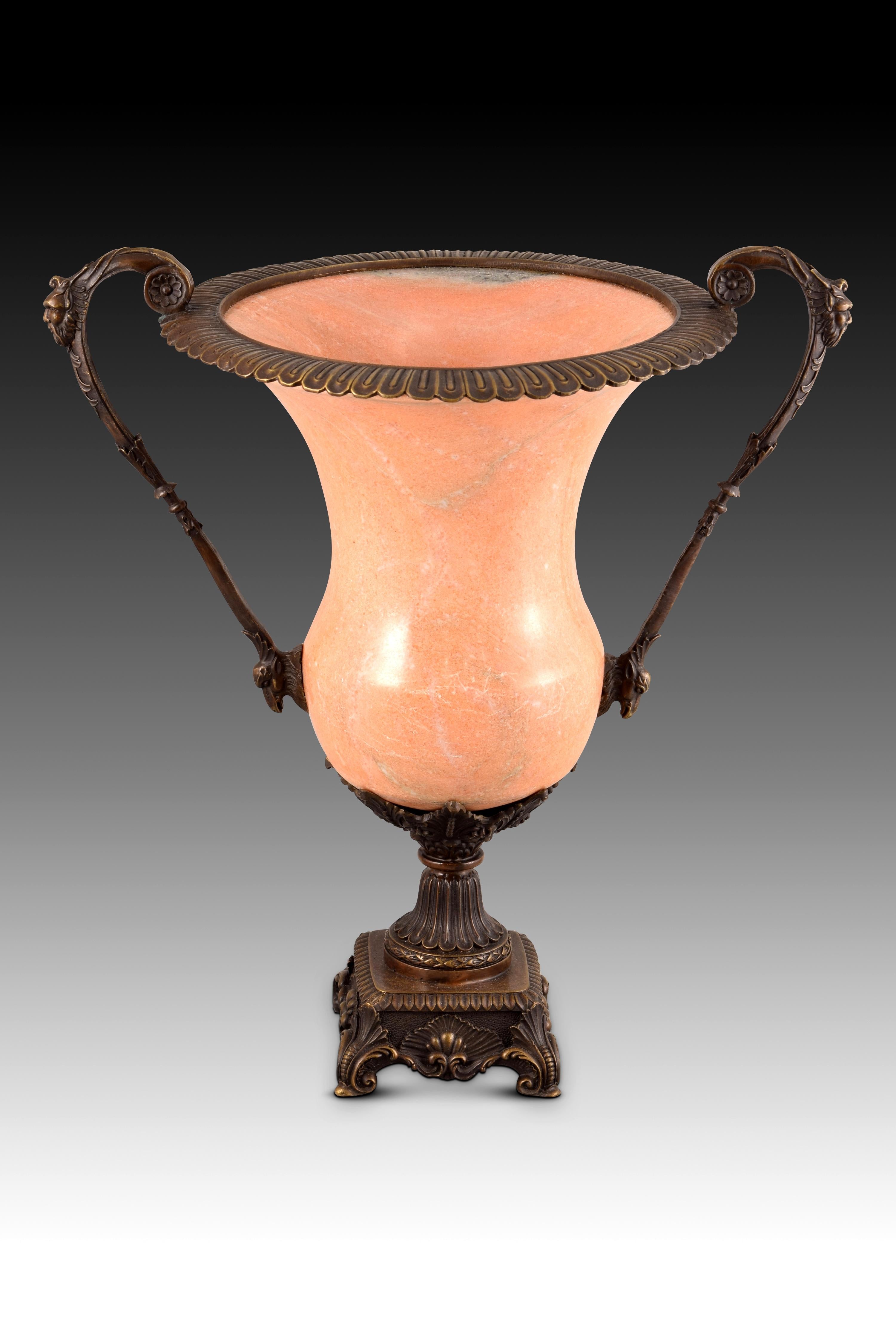 Cup in bronze and marble. Function to the lost wax, 20th century.
On a square base resting on scrolls and decorated with plant motifs stands the cup, made up of a base and handles with bronze masks and leaves and a pink alabaster container. The