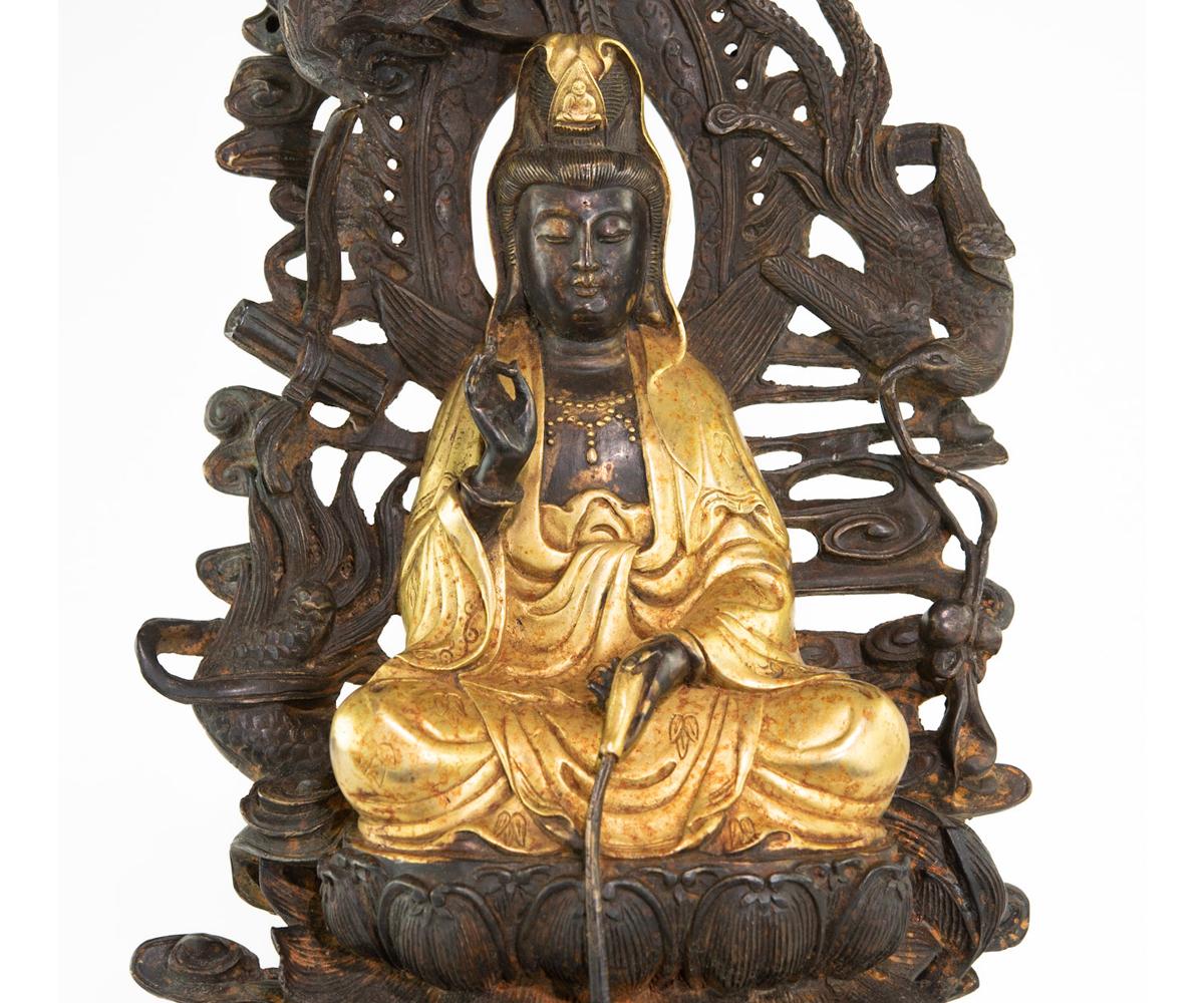 Parcel gilded bronze compassion Quan Yin seated on a double lotus base holding a medicinal willow branch used to cure illness with a half overturned vase resting in her lap. Her halo is decorated with two phoenix, one holding a scroll, another ta