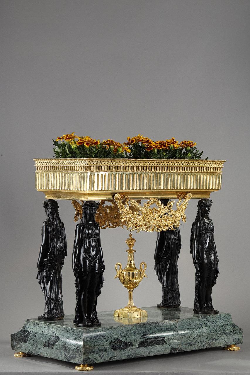 Gilded and patinated bronze planter mounted on a stepped sea-green marble base, with women in long tunics at the corners and a central amphora with swan-shaped handles. Like the columns with female figures on the Erechteion in the Acropolis of