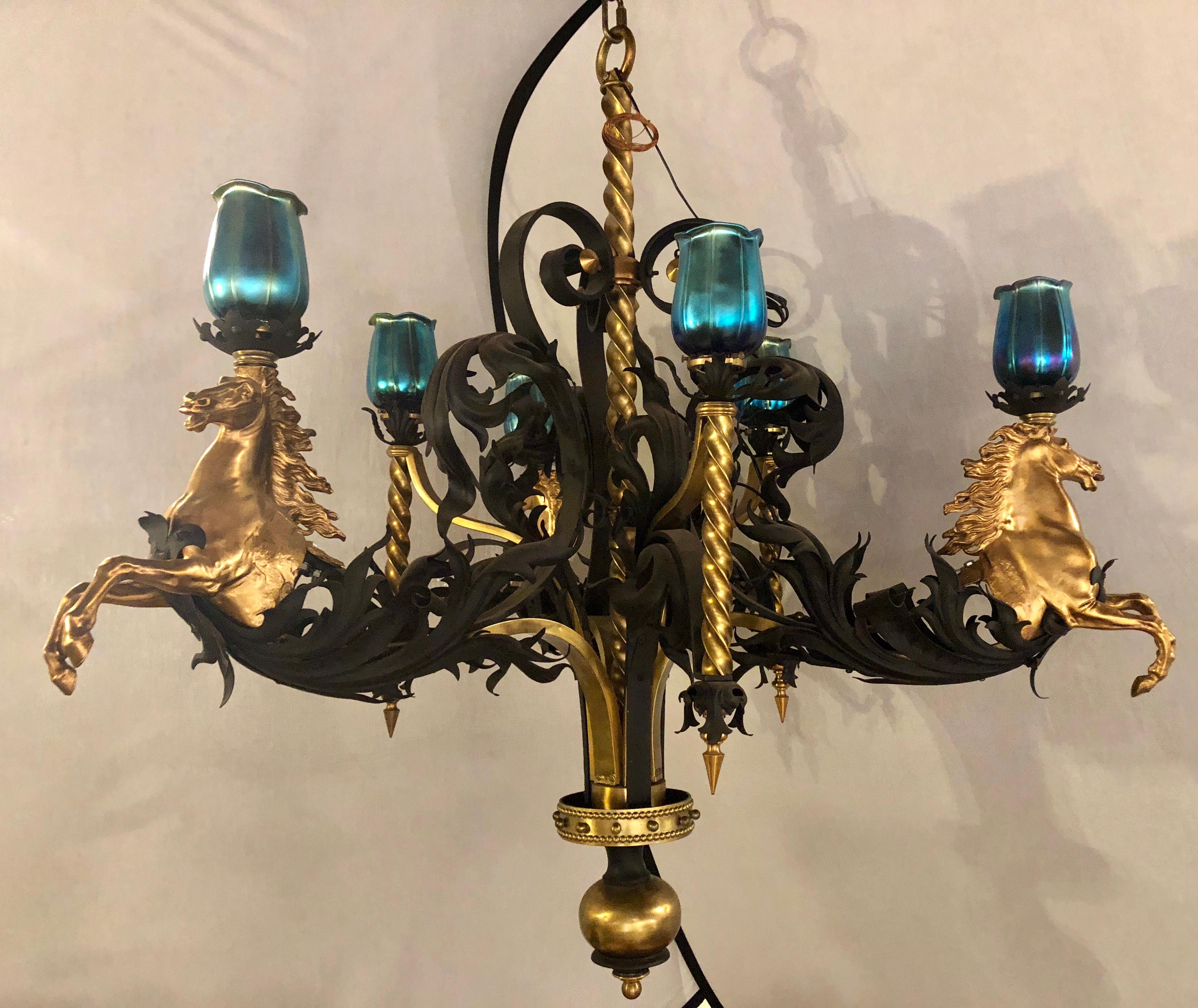 A bronze and wrought iron palatial stallions chandelier with Quezal style shades having six lights. This simply magnificent palatial chandelier would make any men’s room or patio jump over the huddles. The gilt bronze stallions leaping from their