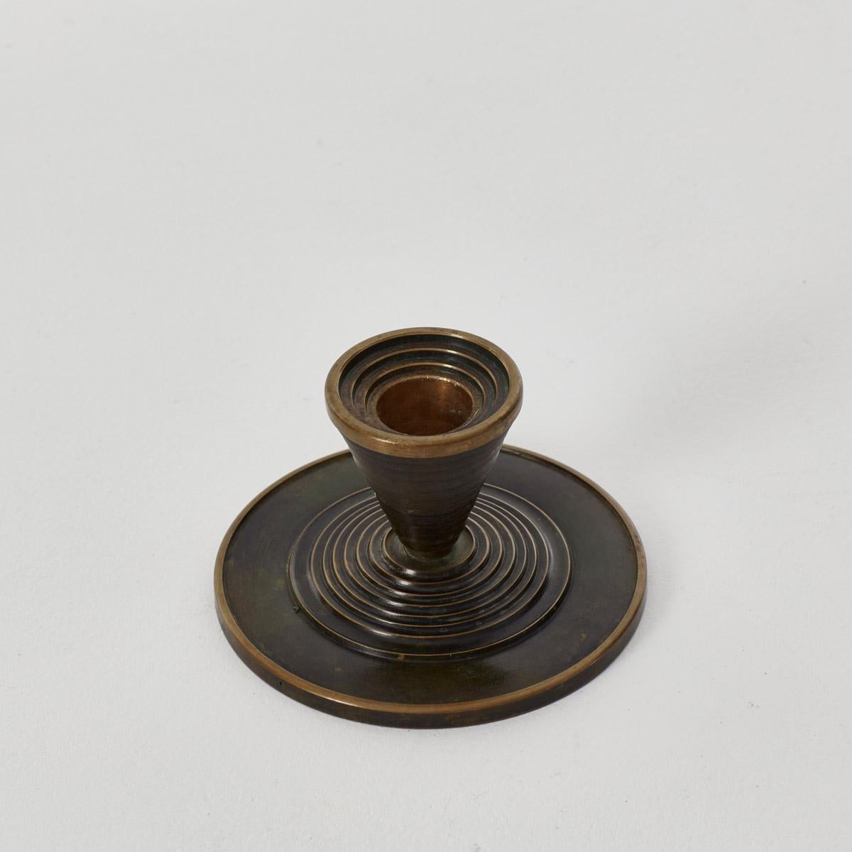 A solid bronze candlestick made in Denmark in the 1920s. With a minimal design it features a conical shape and ringed detail, which ripples across the holder.
 