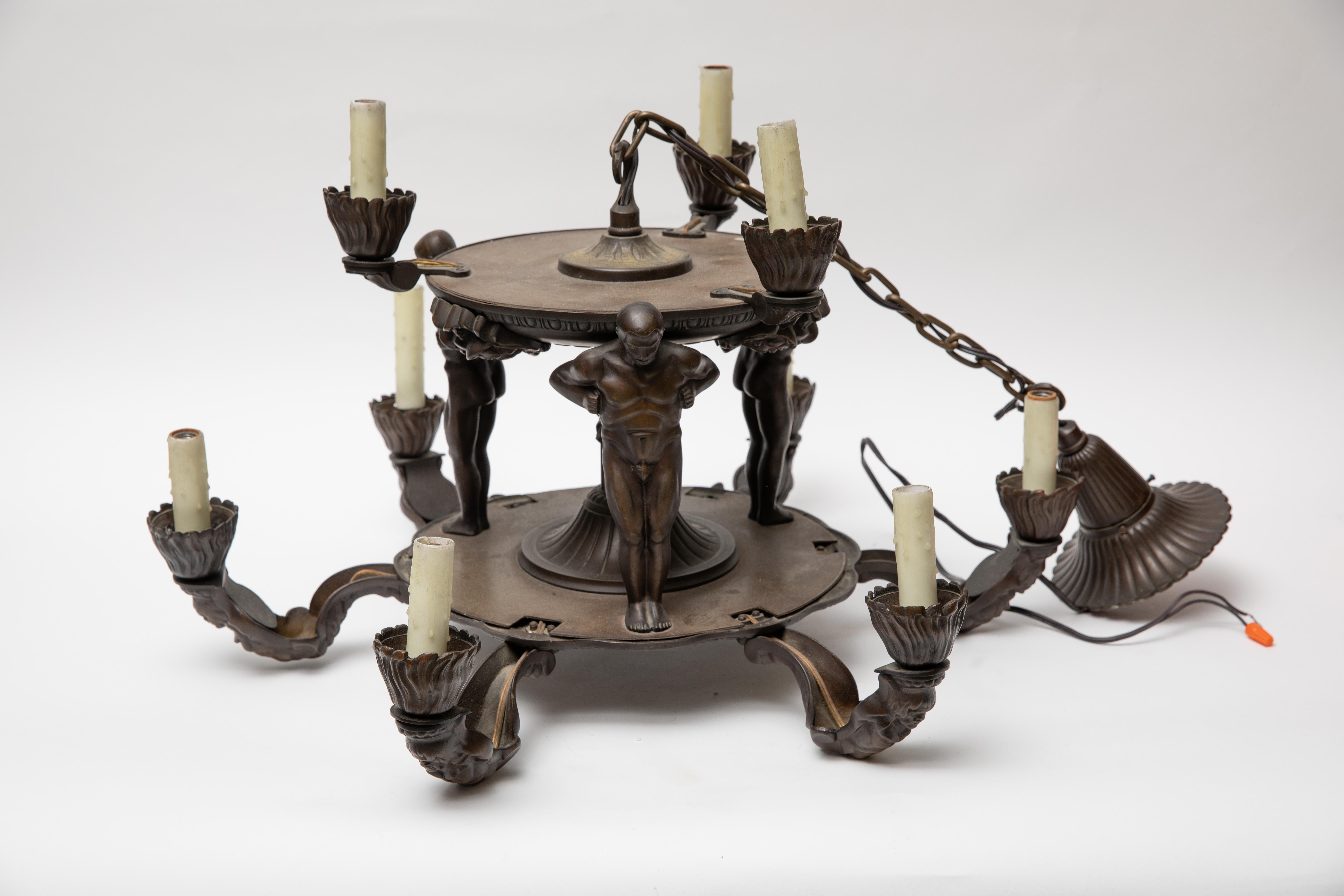 Exceptional bronze Wiener Werkstätte, Gurschner style nine-light chandelier.  Circa 1930. Two tiers having three standing male figures supporting the upper three-light structure, the lower six-light segment with arms embellished with masks and