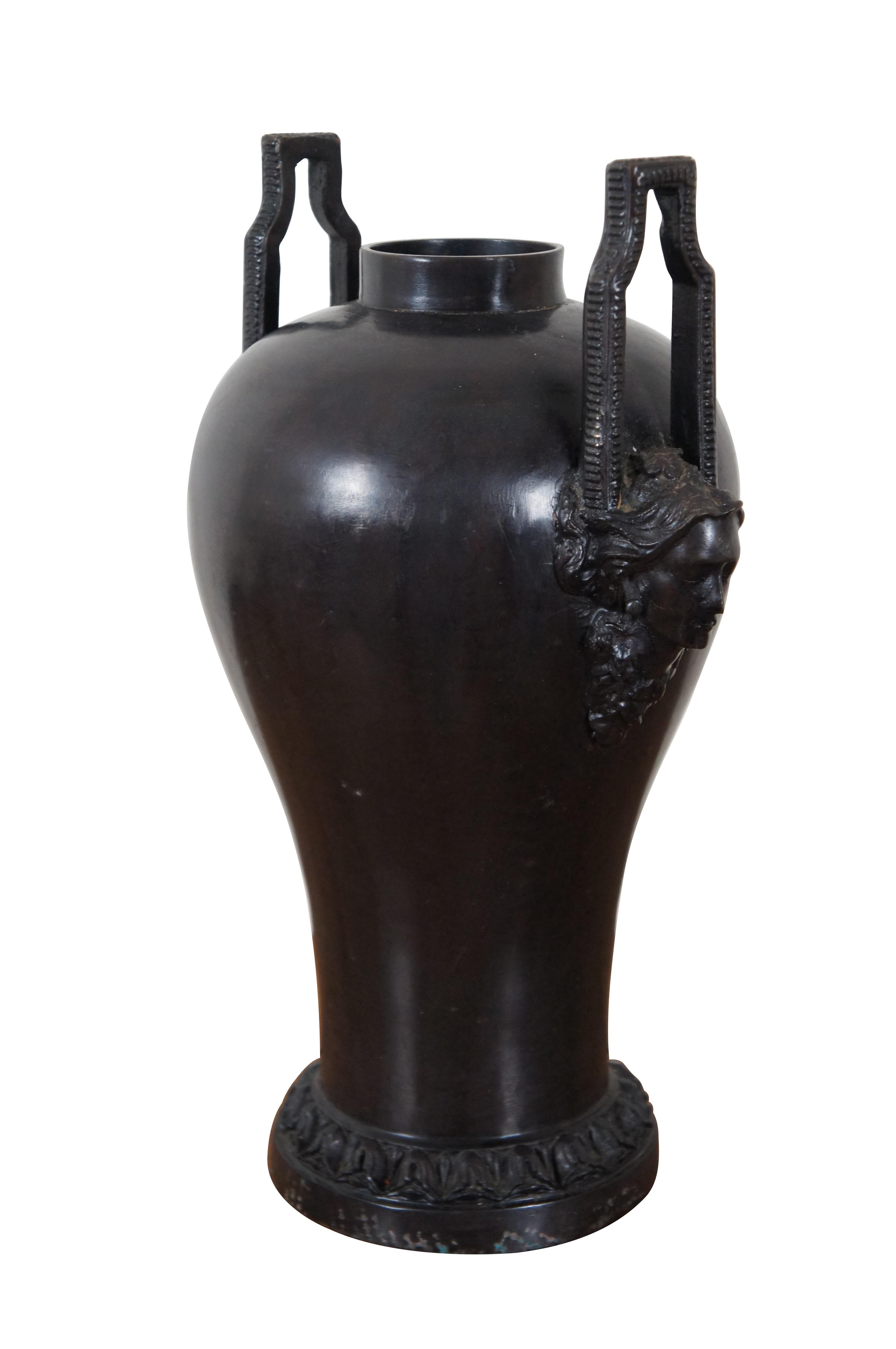 Urne / vase / récipient en bronze de style Art Vintage présentant de hautes poignées en forme de trou de serrure avec une texture striée au-dessus d'une paire de visages de femmes en bas-relief, et un bandeau de feuillage autour de la base.