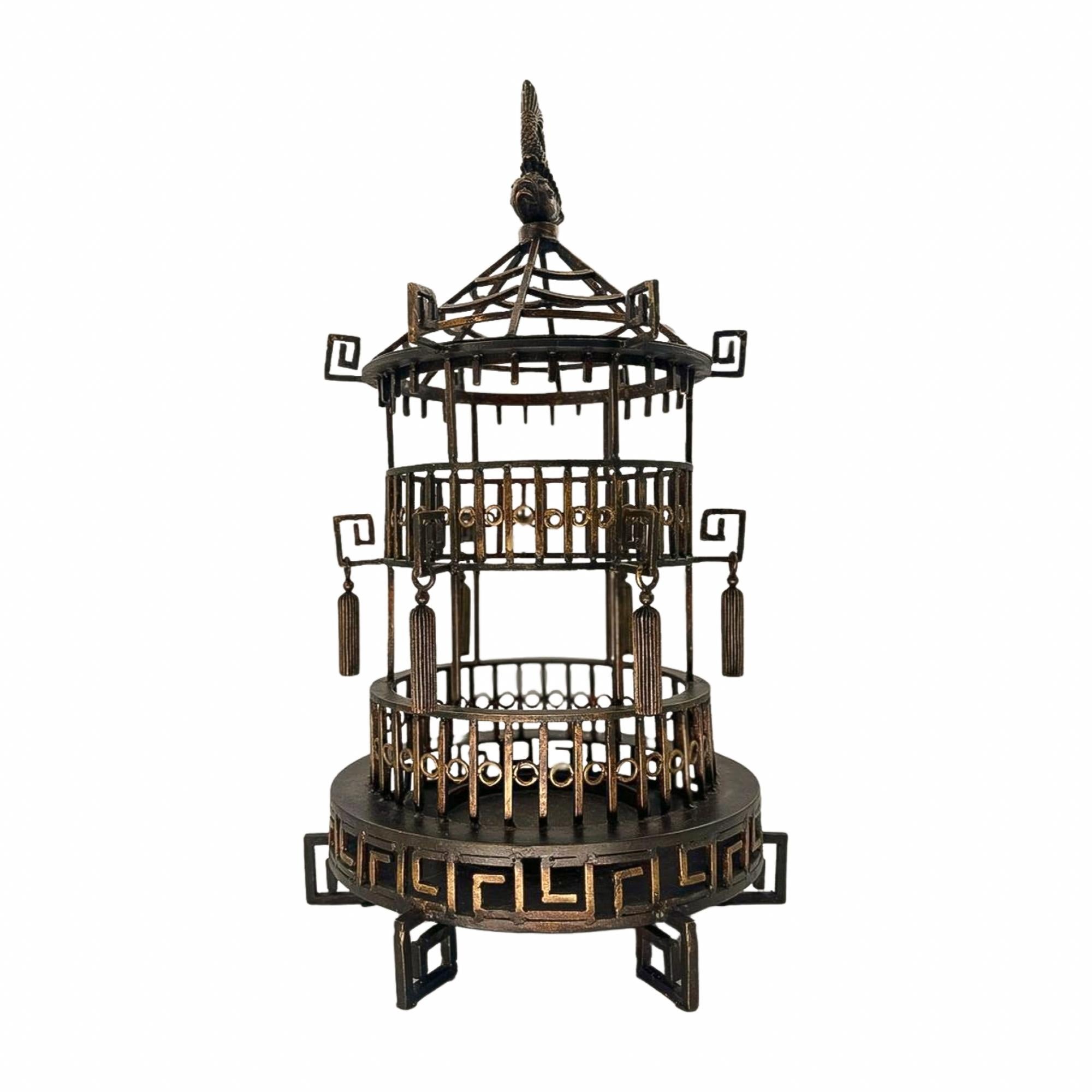 This striking vintage metal pagoda sculpture captures the spirit of chinoiserie design with architectural precision and decorative flair. Crafted in a tiered, openwork form, it features circular balconies, Greek key motifs, and suspended tassel