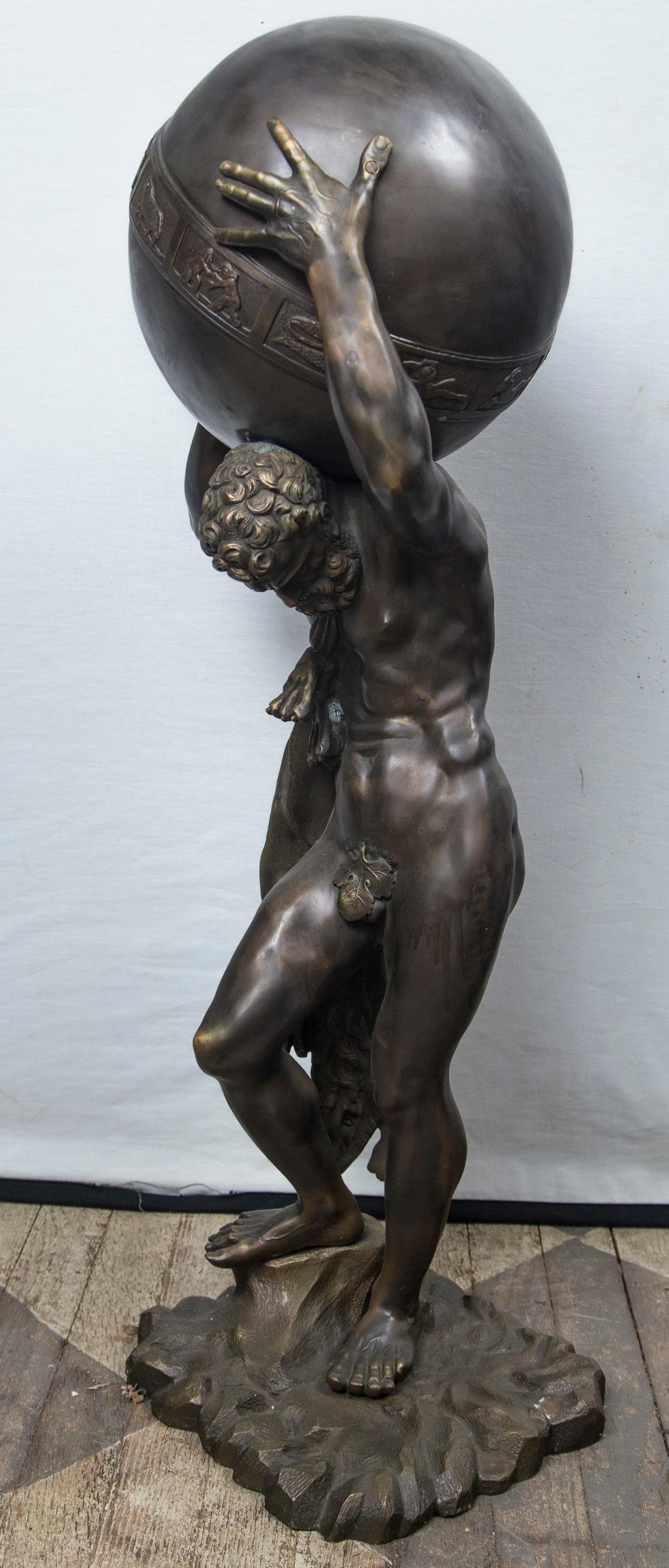 The bronze having a golden brown patina. The draped figure of Atlas holds the globe of the zodiac on his shoulders, his head bent forward. He stands on a rocky base that measures approximately 10 x 10 inches. From extended right elbow the width is