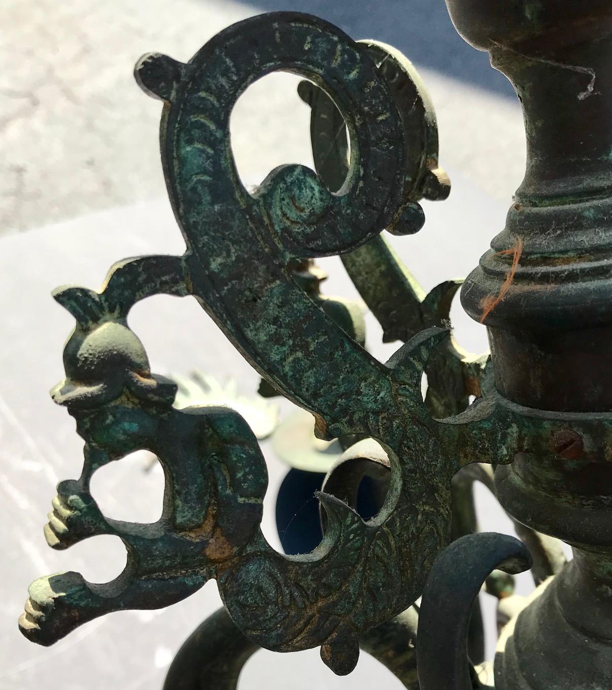 Heavy bronze chandelier with six arms. It has the original dark patina with green shading. The six scrolled arms and the top are decorated with bronze, incised cut outs of legendary Merman figures and wings. 

This chandelier is adjusted to be