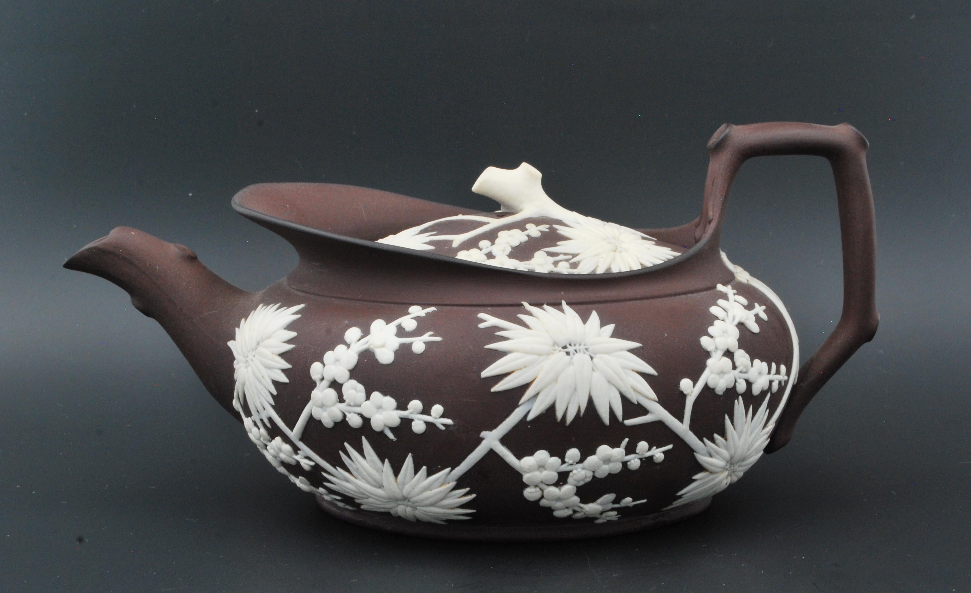 Low oval teapot in ‘chocolate porcelain’, as Wedgwood called this brown stoneware. White applied decoration, to create the appearance of a Japanese bronze.