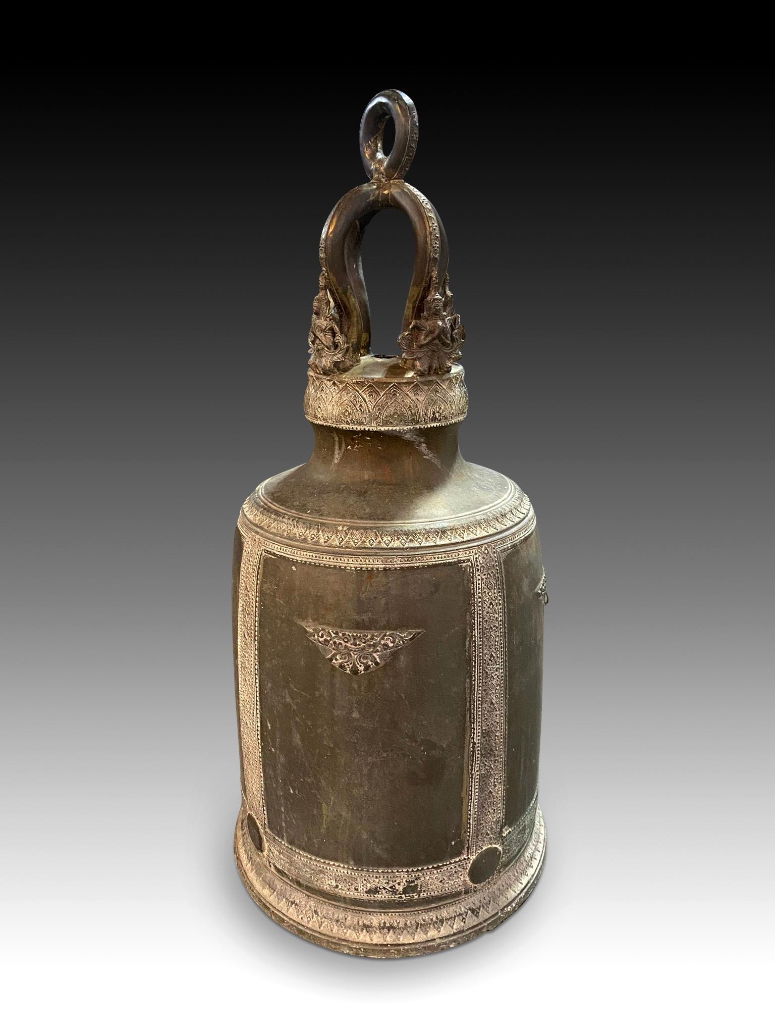 Bronze bell. India, 20th century. 
Bell made of bronze with a tall body and an oval base, almost rectangular in height, which has an elaborate upper part with smooth areas and figures of the same material. In addition to these, it has been decorated