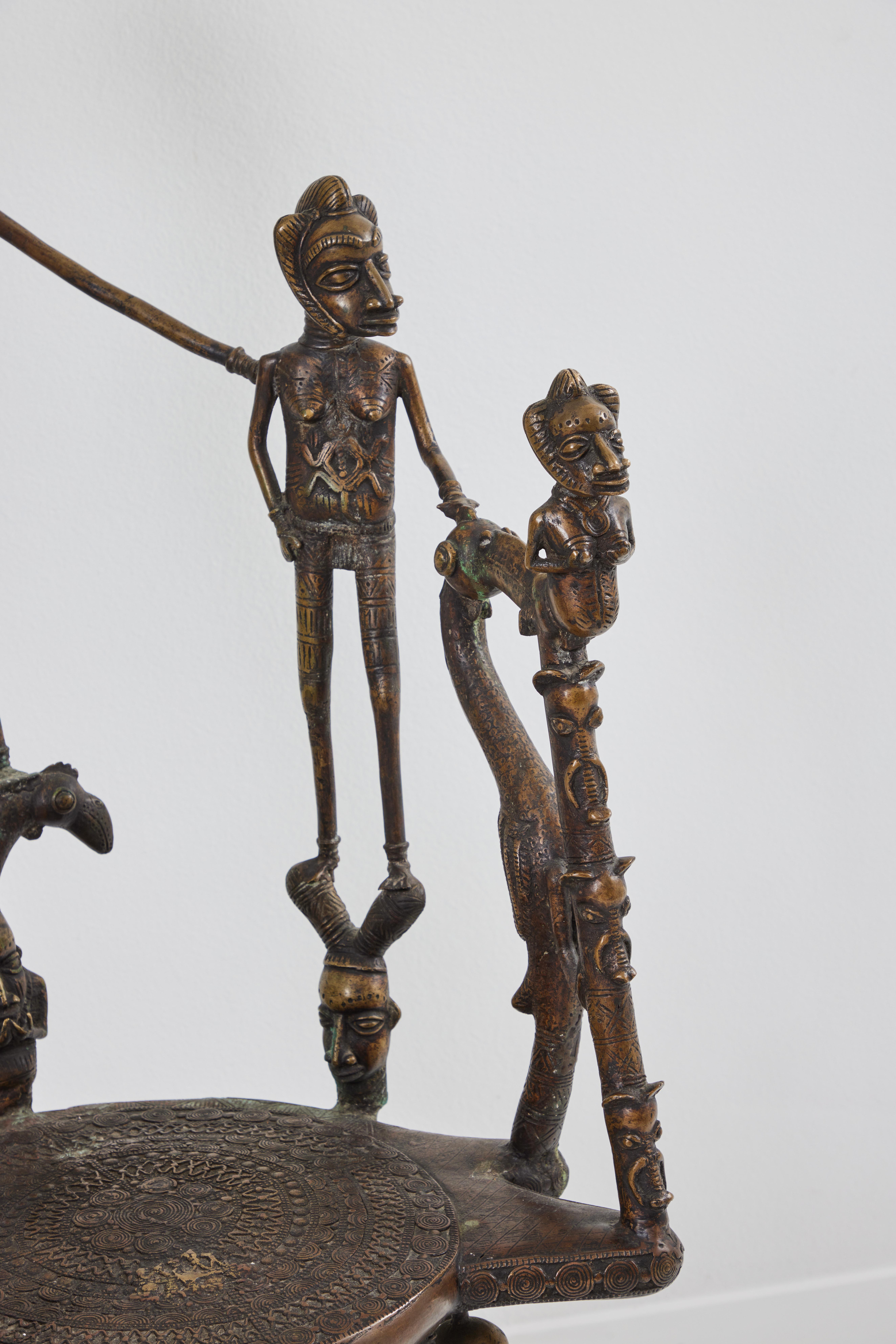 This is a solid cast bronze African throne chair from the country of Benin. Displayed are a head/ lead figure flanked by 4 female figures that support the arms while sitting. One small figure holds up the lead figure while 6 figures support the seat
