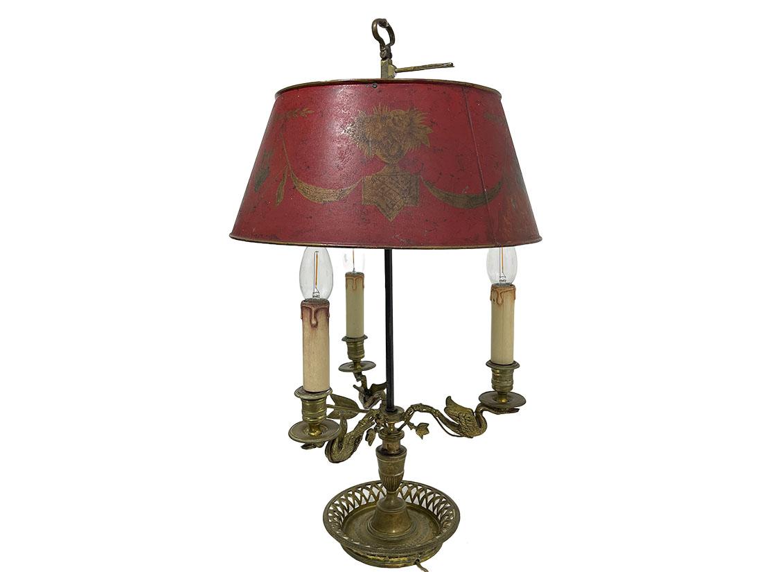 Bronze Bouillotte lamp, France circa 1800.

Bronze Bouillotte Lamp with red and gold painted metal shade, French, circa 1800. Louis XVI lamp with 3 curved arms in the shape of swans with fish-shaped tails on an urn with round drip tray with