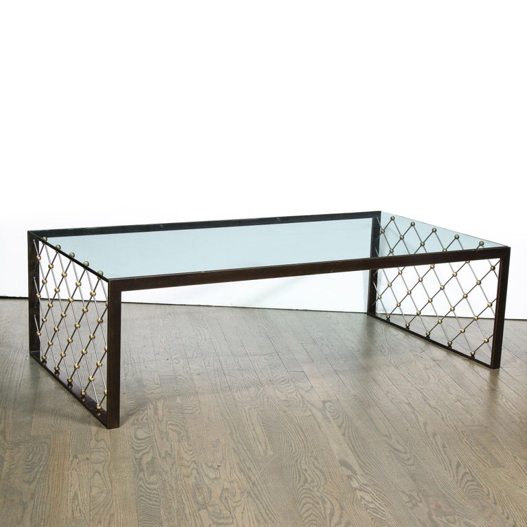 This elegant modernist cocktail table was realized by the esteemed American design firm, Holly Hunt. The piece features a rectilinear oil rubbed bronze frame with lattice work sides in brushed nickel with spherical brass nodules at their