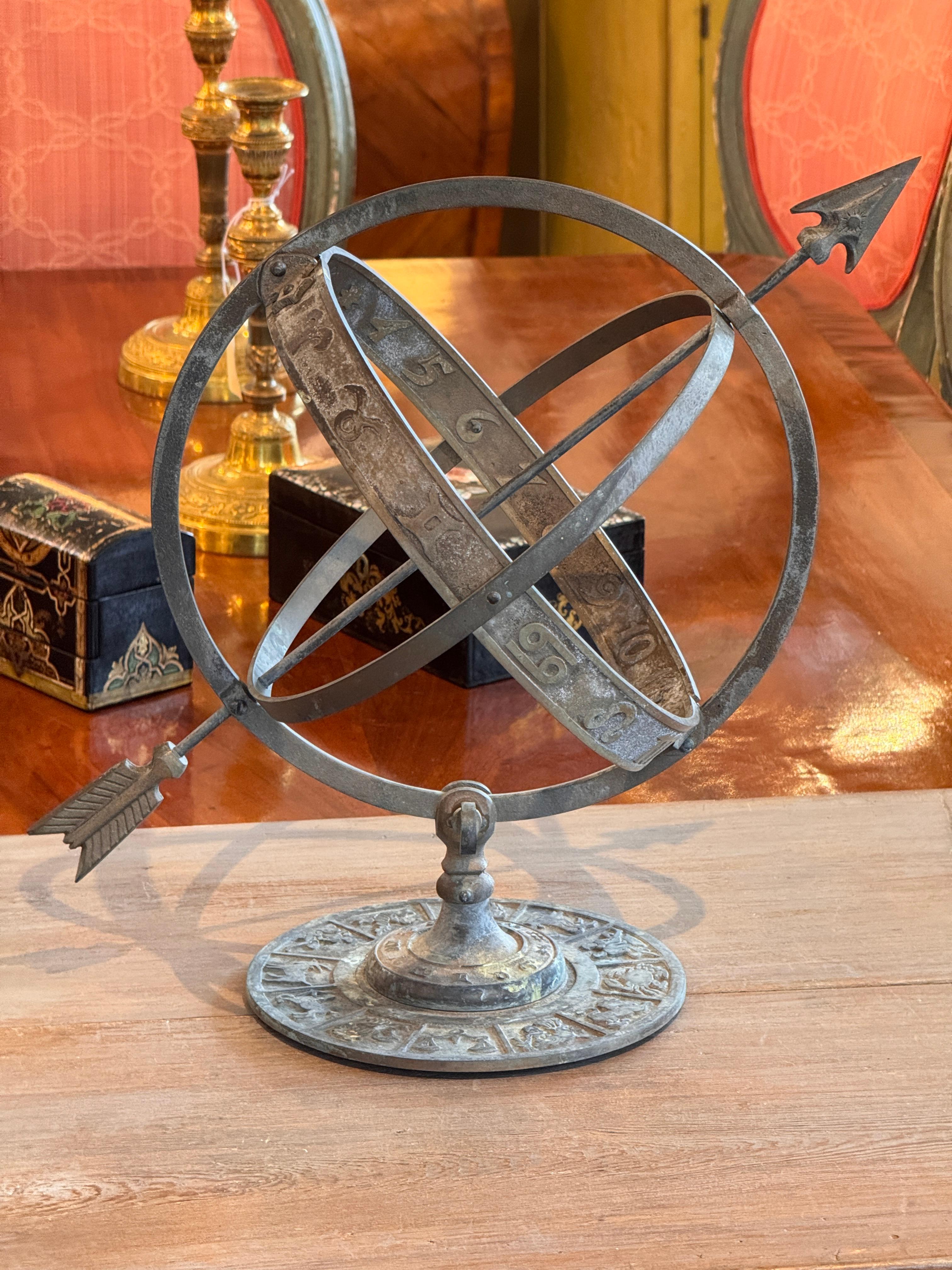 Sphère armillaire en bronze vintage présentant des anneaux classiques entrelacés, un axe de flèche et une base circulaire détaillée ornée de motifs du Zodiac. La finition patinée ajoute de la profondeur et du caractère à cette forme astronomique