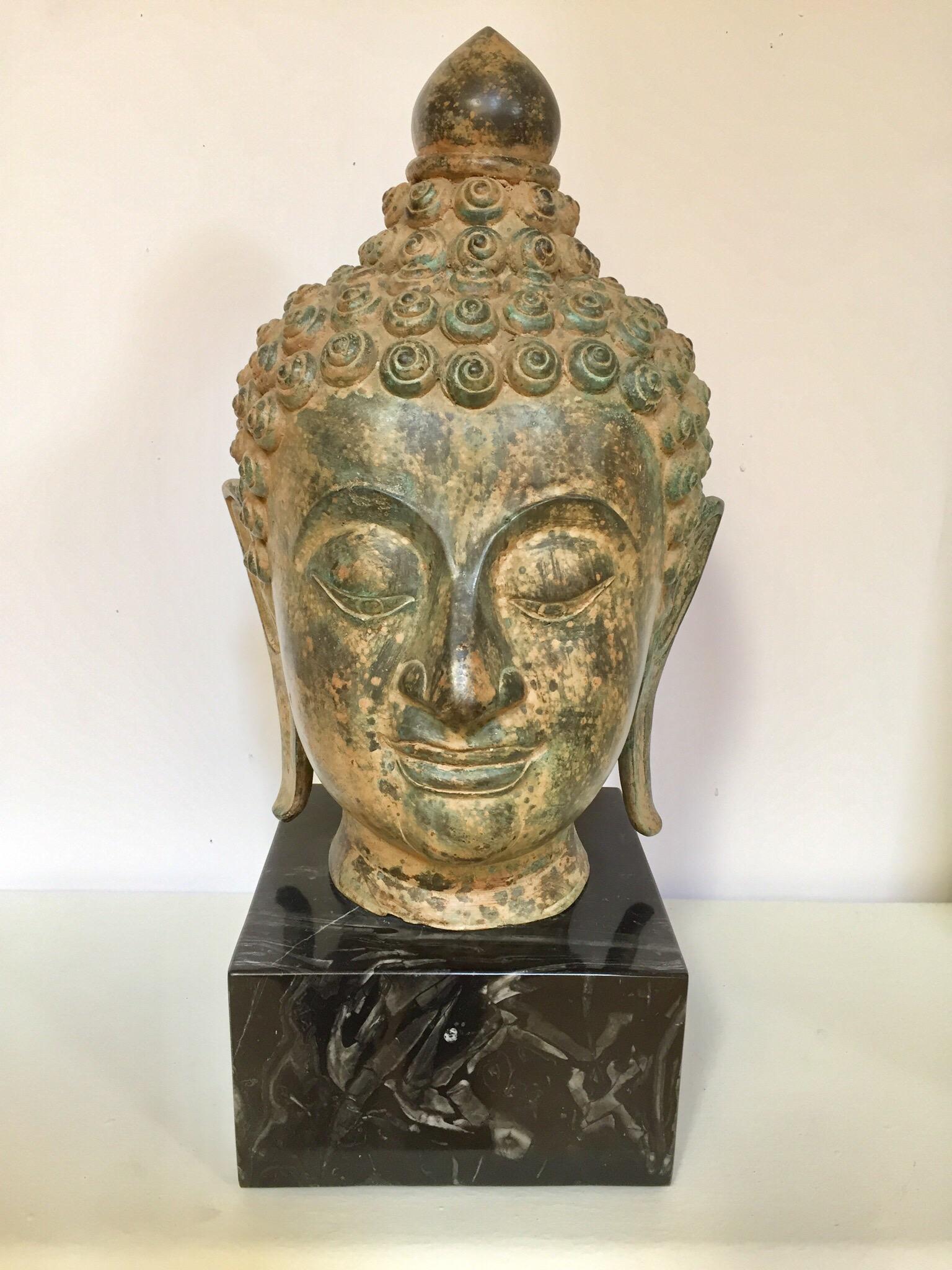 Life-size bronze Buddha head sculpture mounted on marble stand.
Buddha head with eyes lowered in meditation, serene and calm, representing the enlightened Buddha.
Finely modeled with incised chin, bow-shaped mouth, elongated eyes and gently