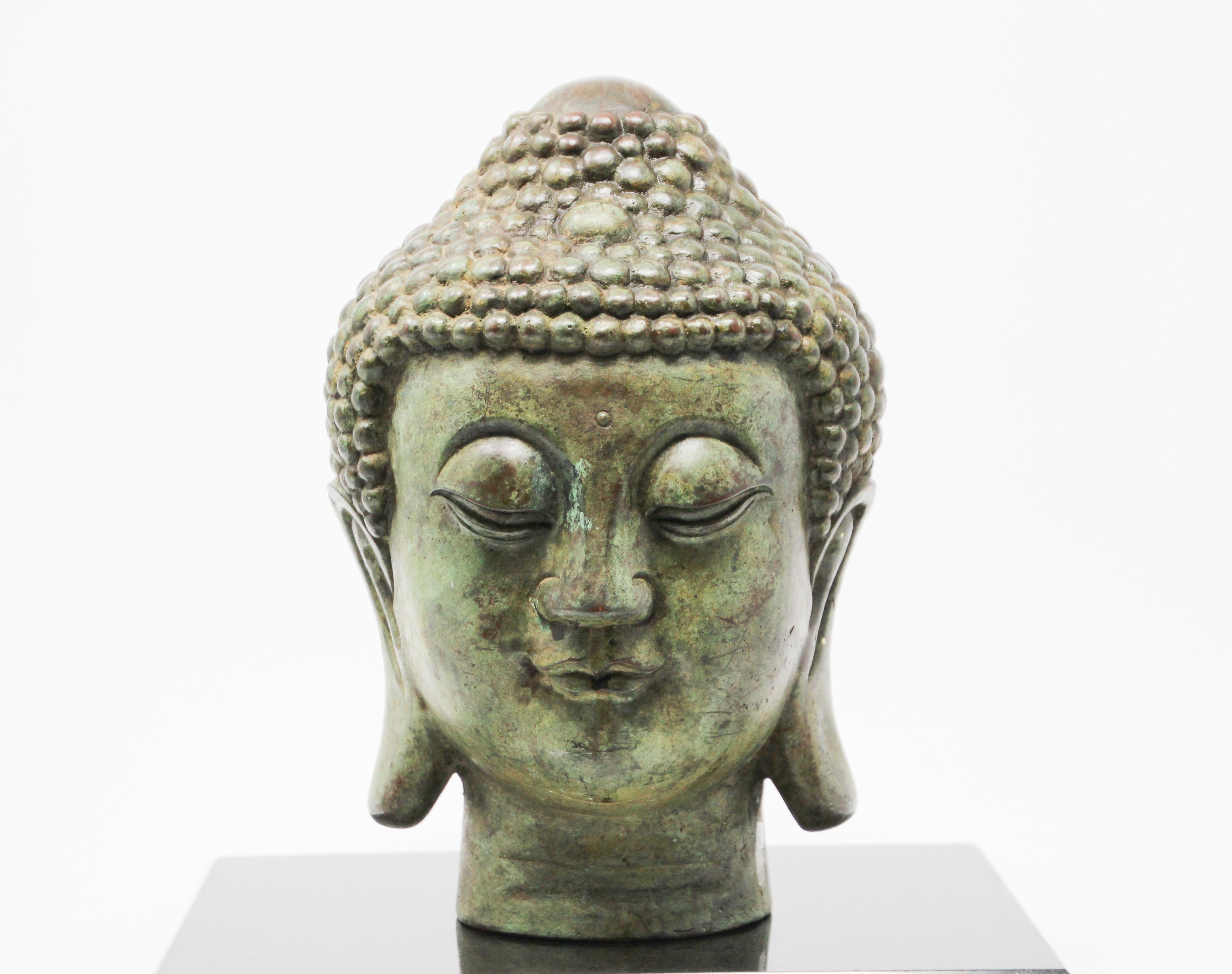 Bronze Buddha head sculpture on marble stand.
Buddha head with eyes lowered in meditation, serene and calm, representing the enlightened Buddha.
Finely modeled with incised chin, bow-shaped mouth, elongated eyes and gently arching brows, flanked