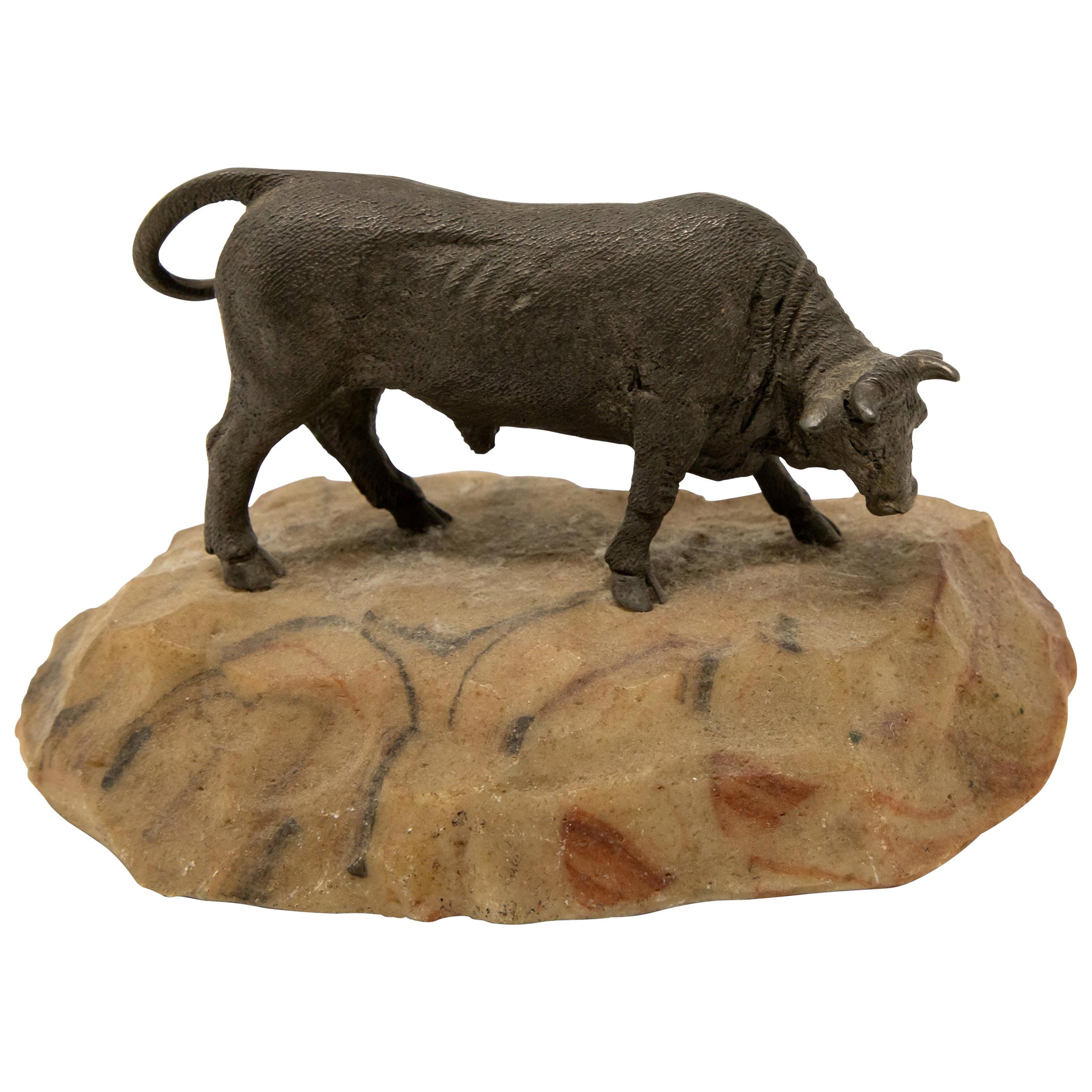 Offering this sculpture of a bronze bull on stone base. Starting with the base is a sand colored stone with some airbrushed reds and blacks. Mounted is the bronze bull with his tail swinging and head down.