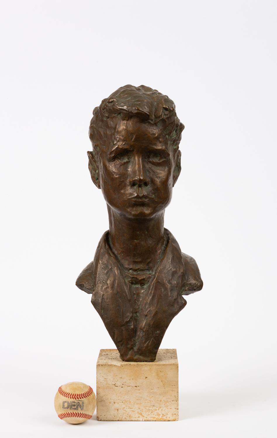 A likeness of a young man or teen with a mid-20th century hairstyle and clothing, rendered in high detail and cast in bronze. The figure is cantilevered along the lapels of its jacket, and bolted to a square base of travertine limestone. The