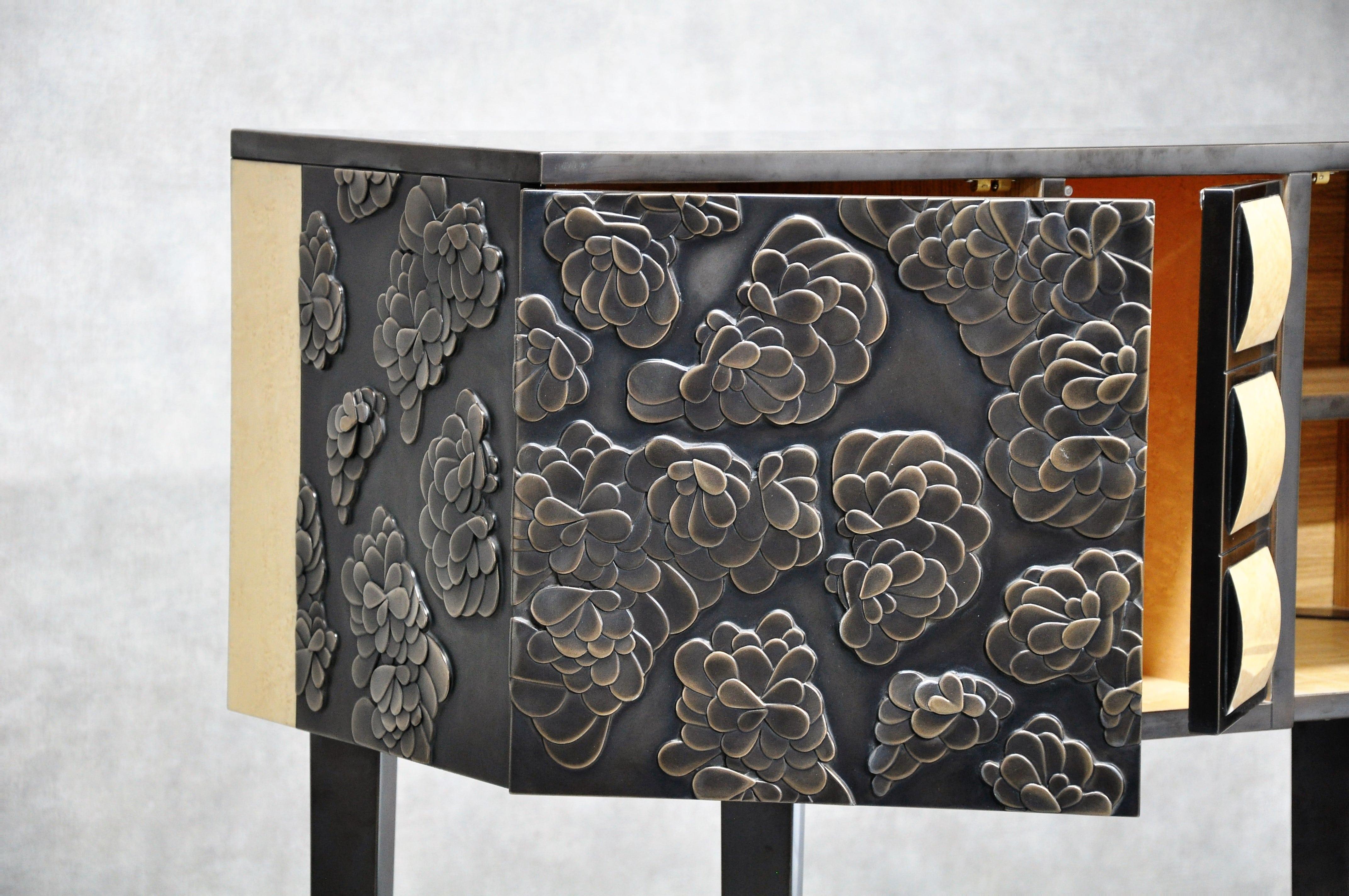 This credenza is clad entirely in thin bronze leaf. The cladding that covers the floral motifs sculpted in the wood is weathered and polished to lend depth. Two doors conceal shelved compartments. The inside of the credenza is made of solid oak and