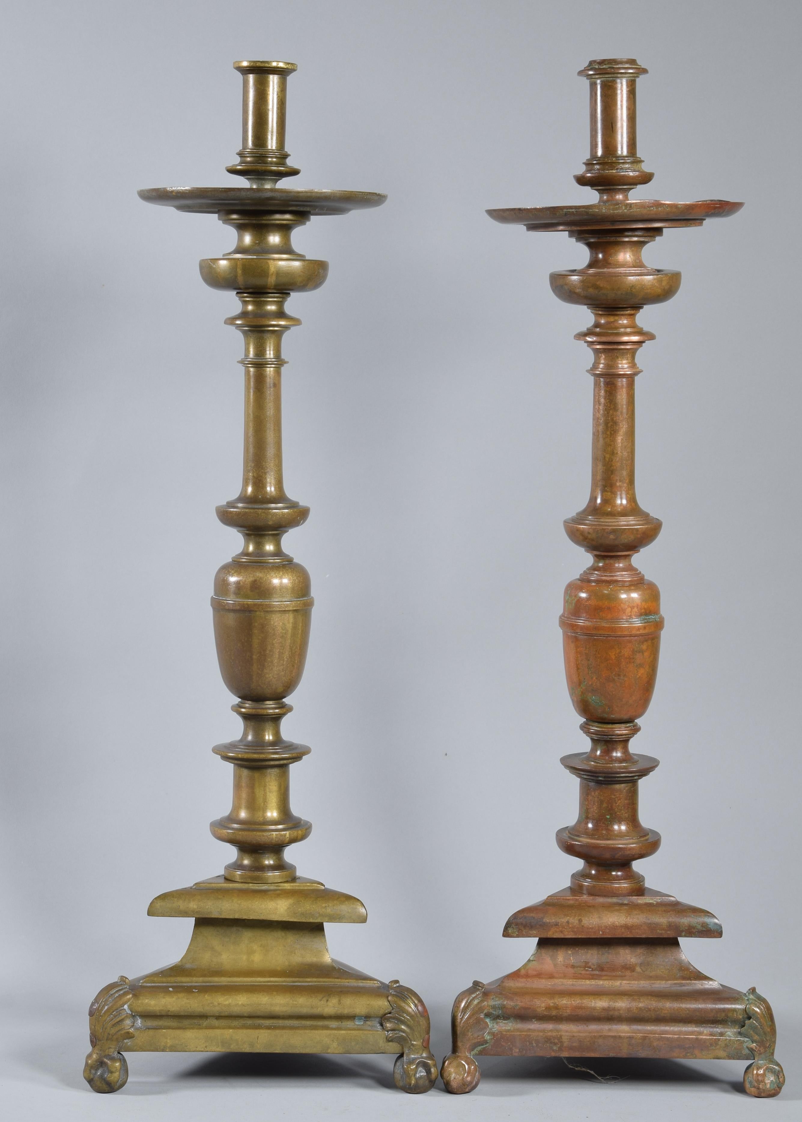 Two bronze candlesticks. Twentieth century. 
 Two practically equal bronze candlesticks with a triangular base on legs (these with vegetal elements finished in claws holding balls) and a vase-shaped shaft finished in a disk from which the piece for