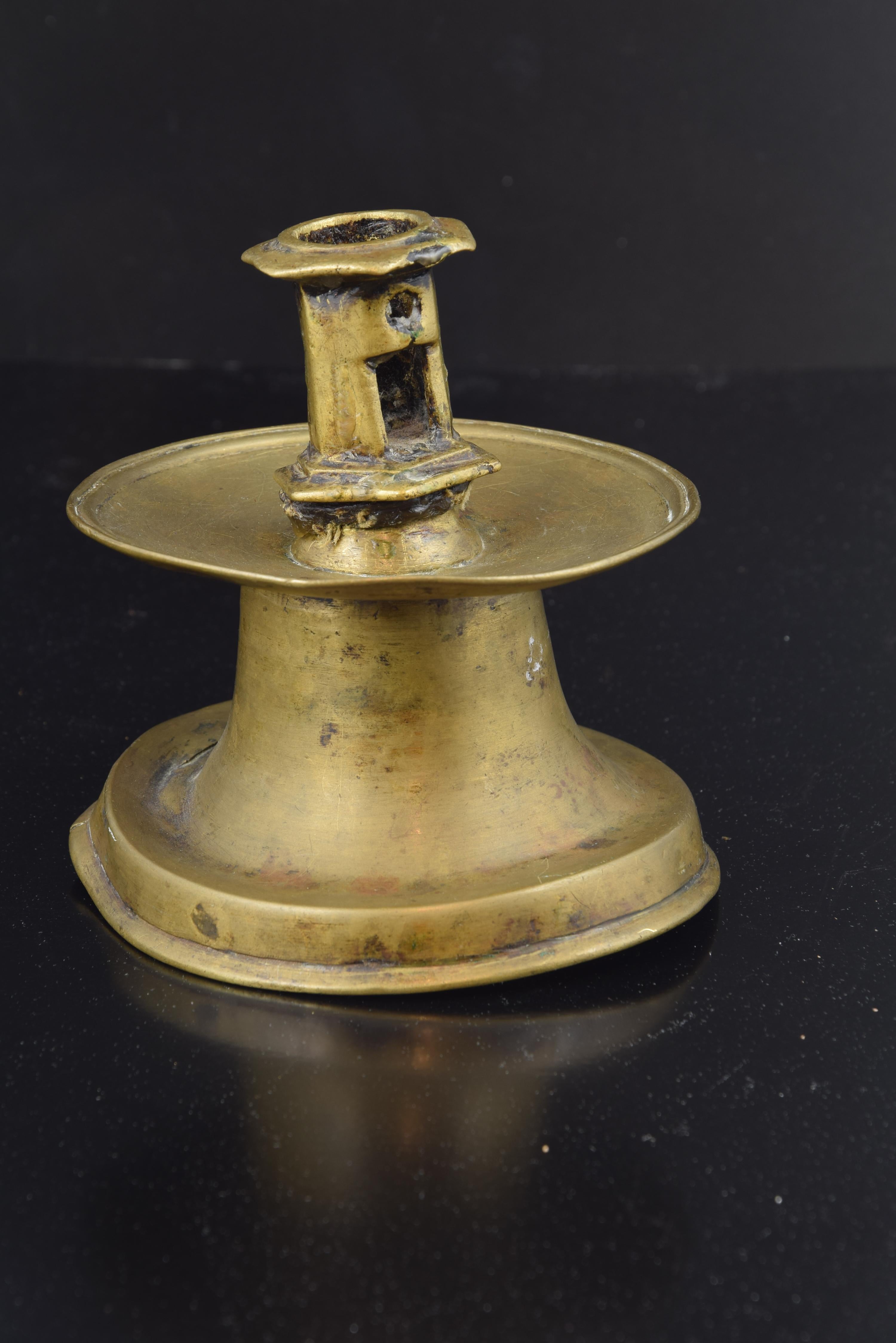 Bronze candlestick. Century XVI.
 Polished bronze candlestick with a wide circular base from which arises a truncated cone axis opening into a smooth plate that houses the candle holder (this one with a polygonal shape and moldings). From the