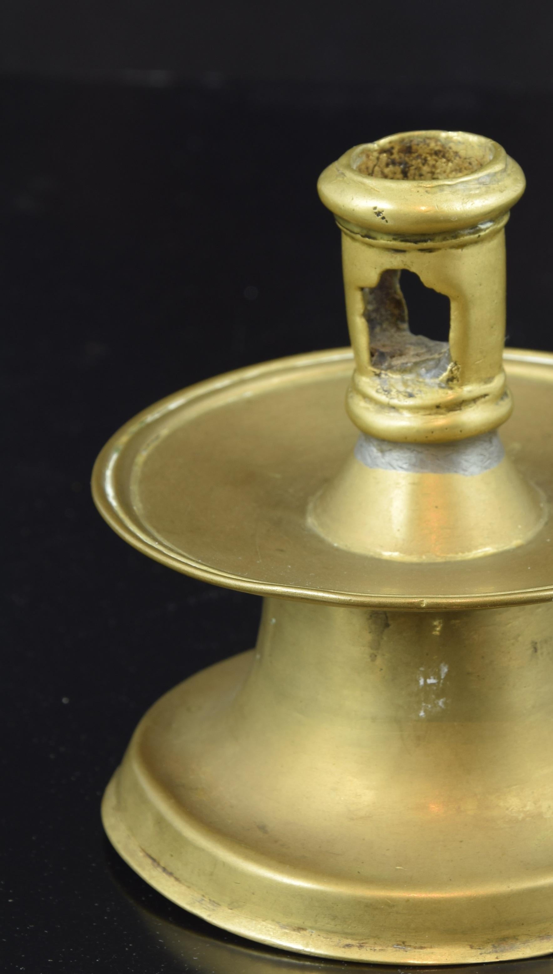 Bronze candlestick. Century XVI.
 Polished bronze candlestick with a wide circular base from which arises a truncated cone axis opening into a smooth plate that houses the candle holder (this one with a polygonal shape and moldings). From the