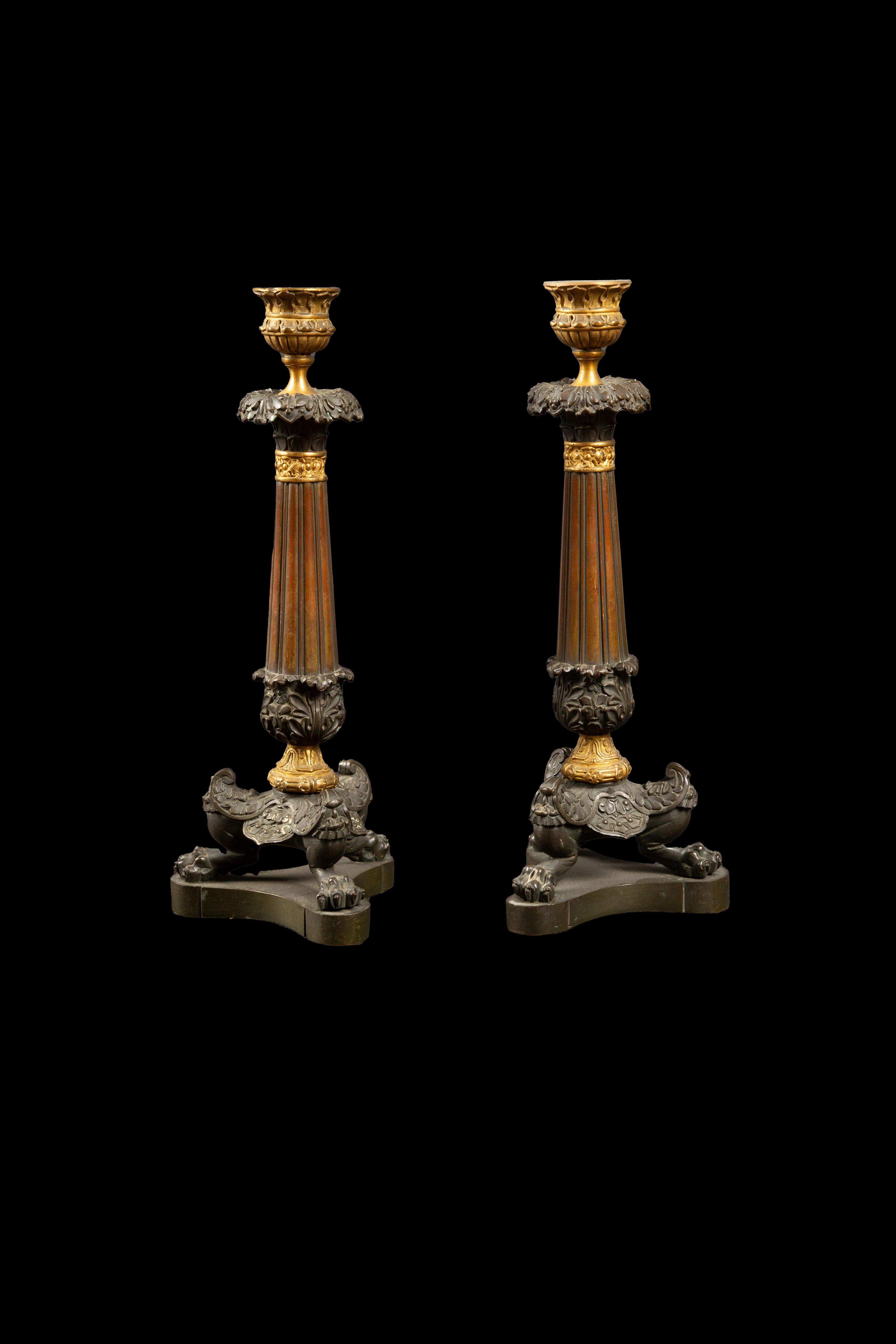 Early 19th Century pair of partially gilt bronze candle sticks with a acanthus leaf decoration, terminating in tripod lion's paw feet.