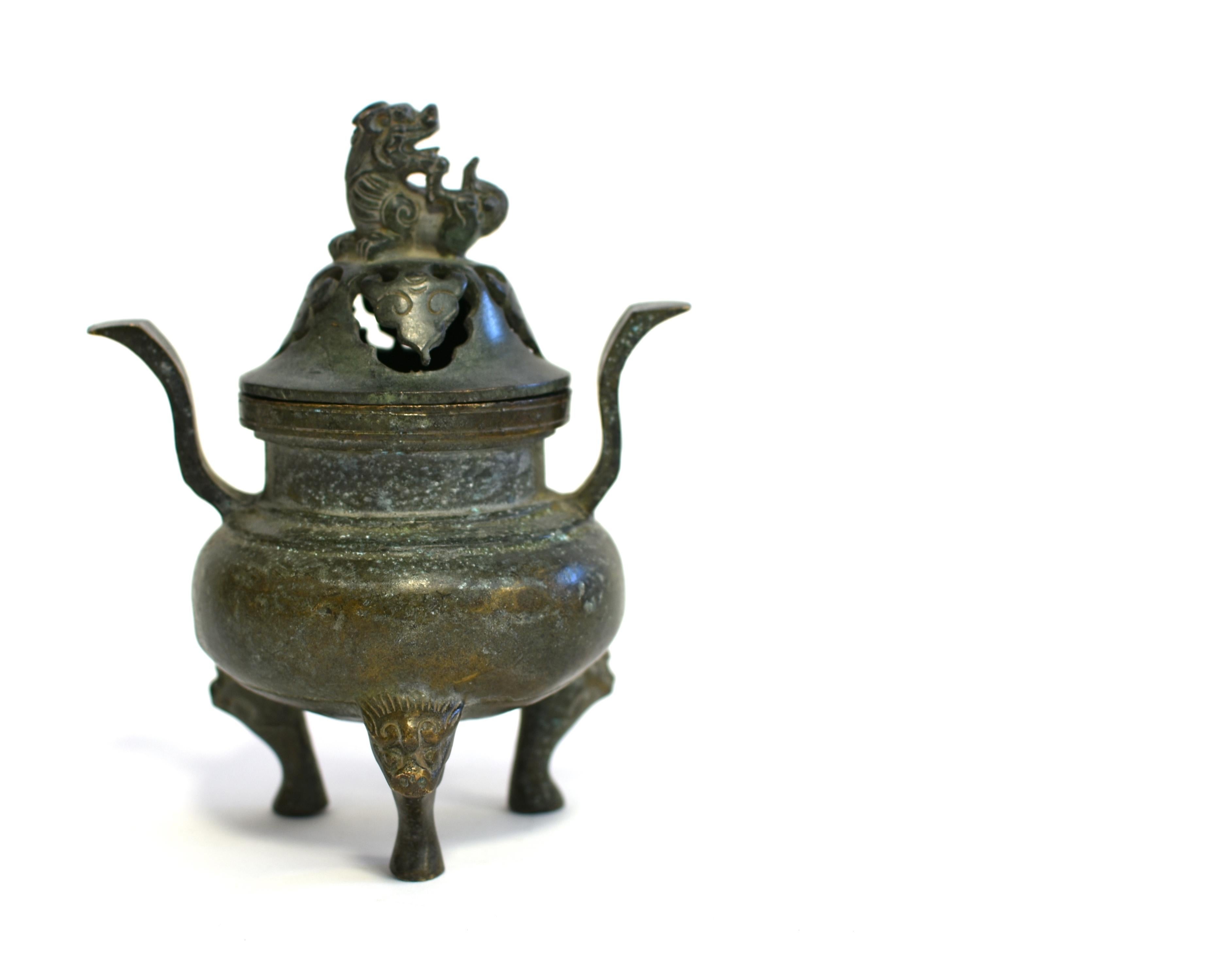 A beautiful antique bronze incense burner in the Ming dynasty style. The vessel's bulbous sides are free of decorations, below two curved upright handles and supported on three animal-form feet issuing from lion masks. The cover is pierced with a