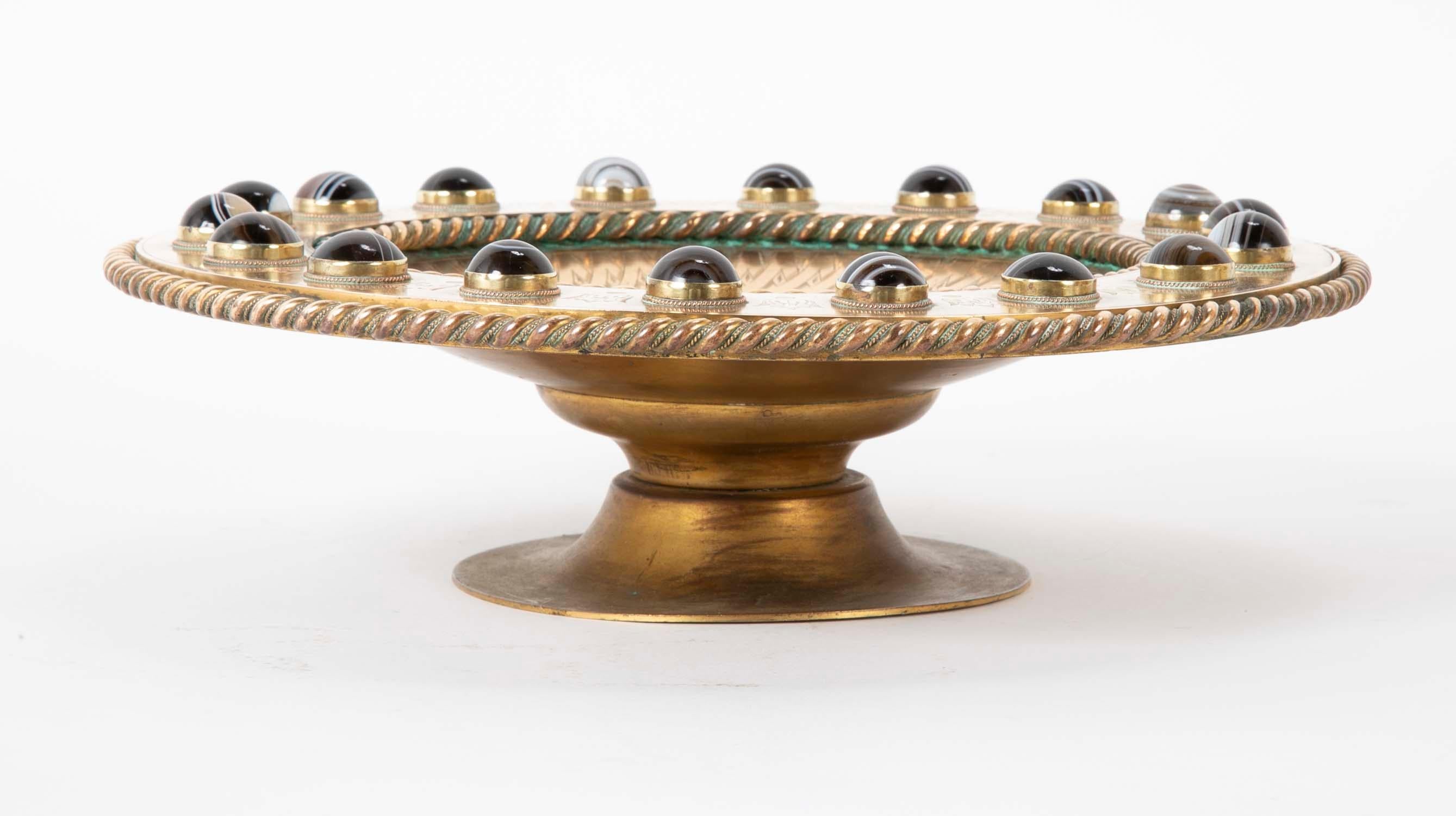 An English or Scottish polished bronze footed tazza with eighteen banded Scottish agate cabochons bezel set at the wide rim. The fabulous shallow-footed bowl has an incised overlapping detail at the top rim of the bowl and braided edges at the wide