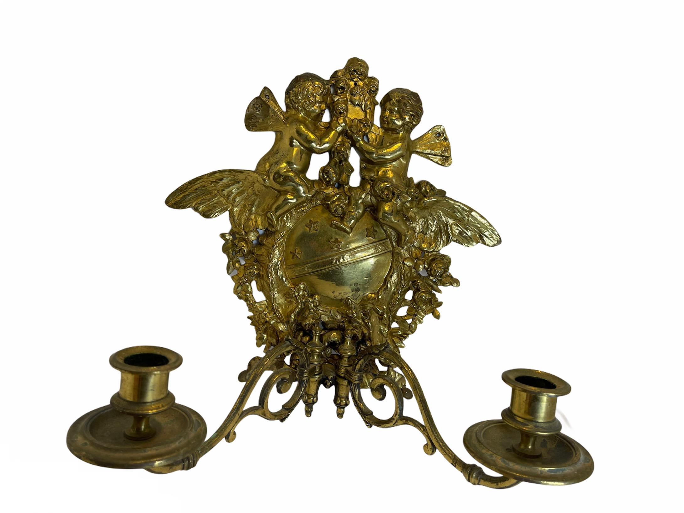 Bronze sconce decorated with a pair of winged cherubs sat over two feathers moon with the stars. It appears that they are adorning the moon with a garland of roses. Two delicate scrolled arms come out from the bottom of it and form the