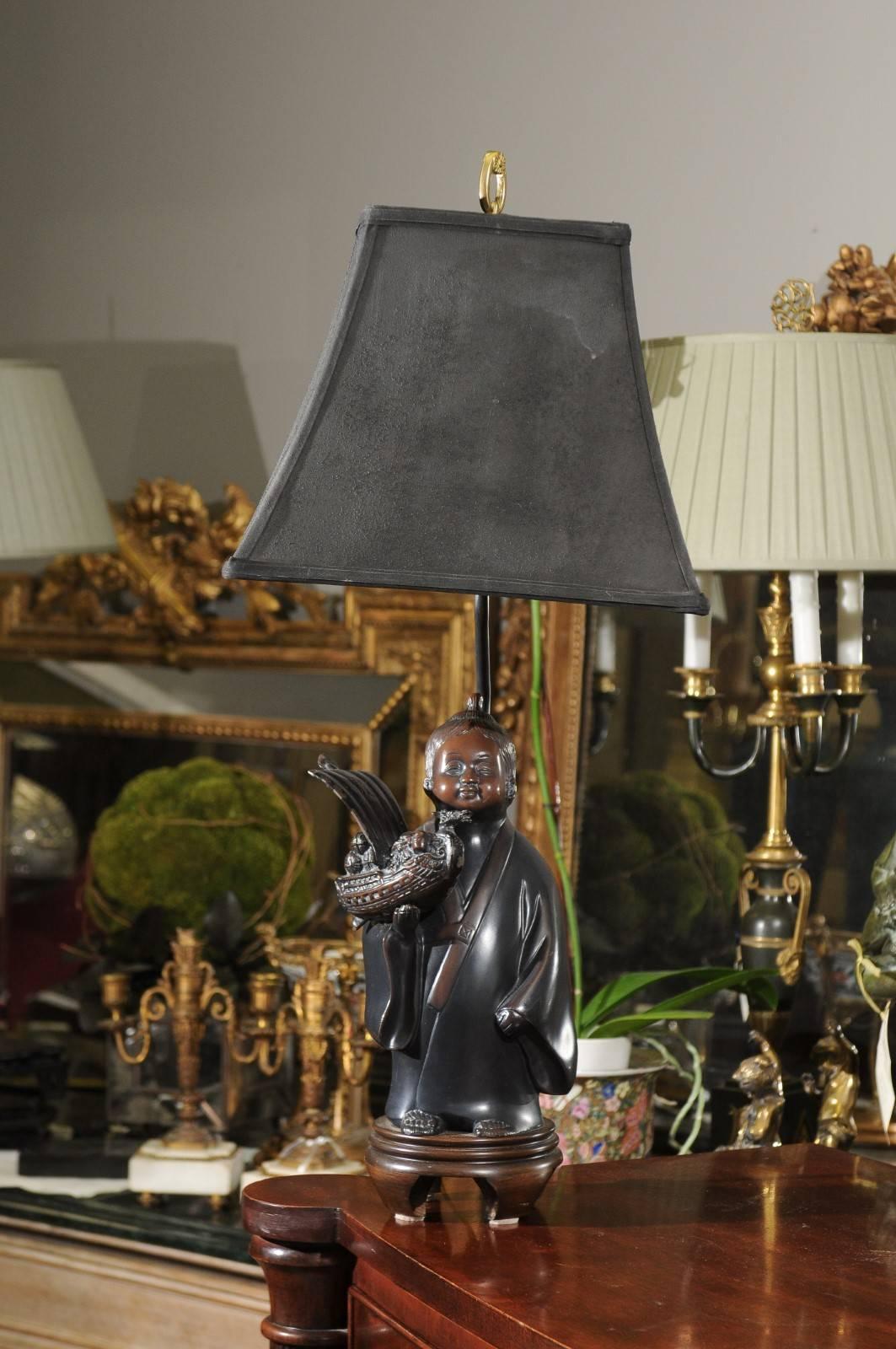 A handsome lamp with a Chinese figure holding a dragon boat mounted to a wooden base. The actual figure in 12 1/2 in. tall and the lamp is 29 in. to the finial.
The black parchment shade is 12 1/2 in. W x 10 1/4 in. H.