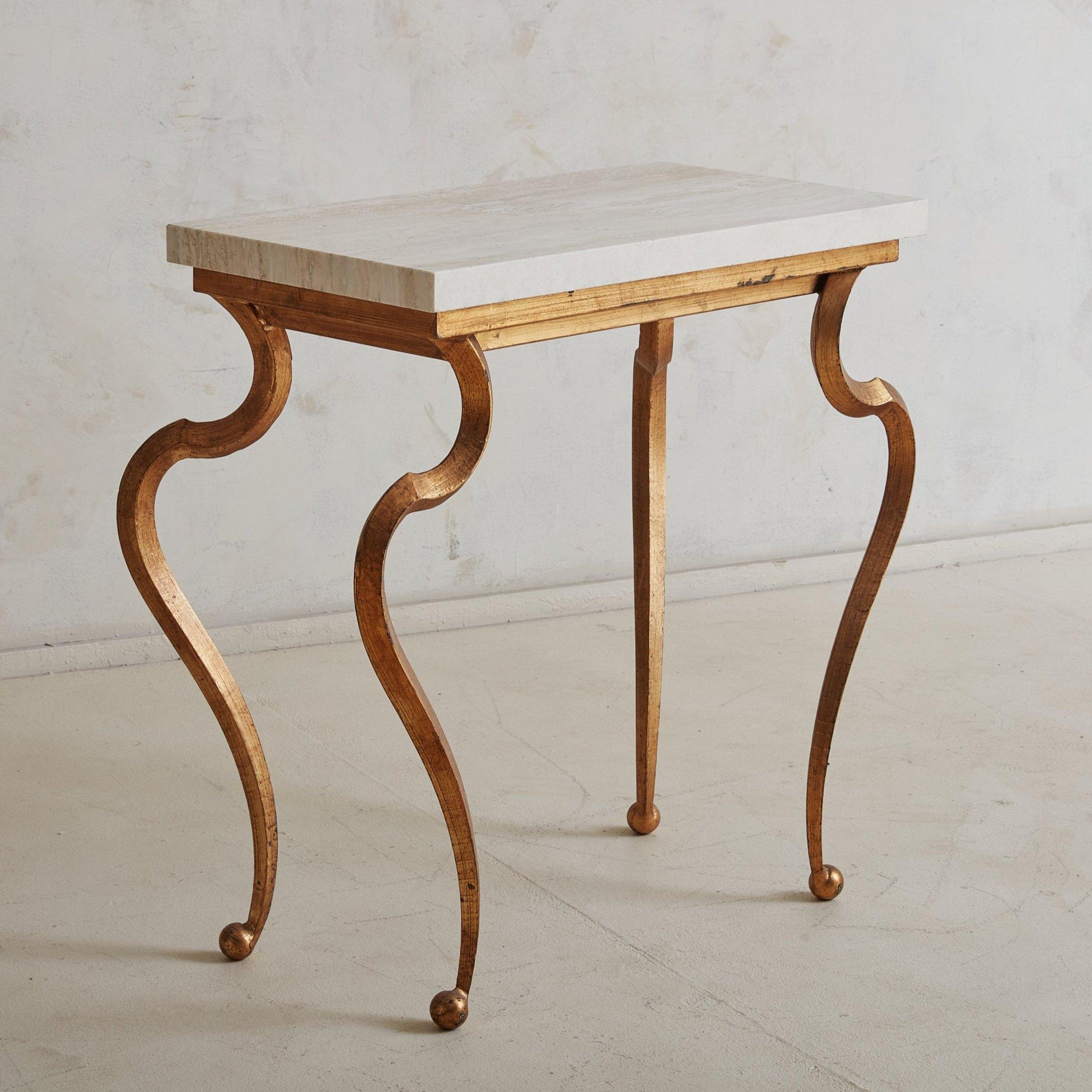 A vintage French console table featuring a gold painted bronze base with dramatically curved cabriole legs and petite ball feet. This piece has a thick rectangular travertine top with gorgeous movement in a range of taupe hues. We can envision this