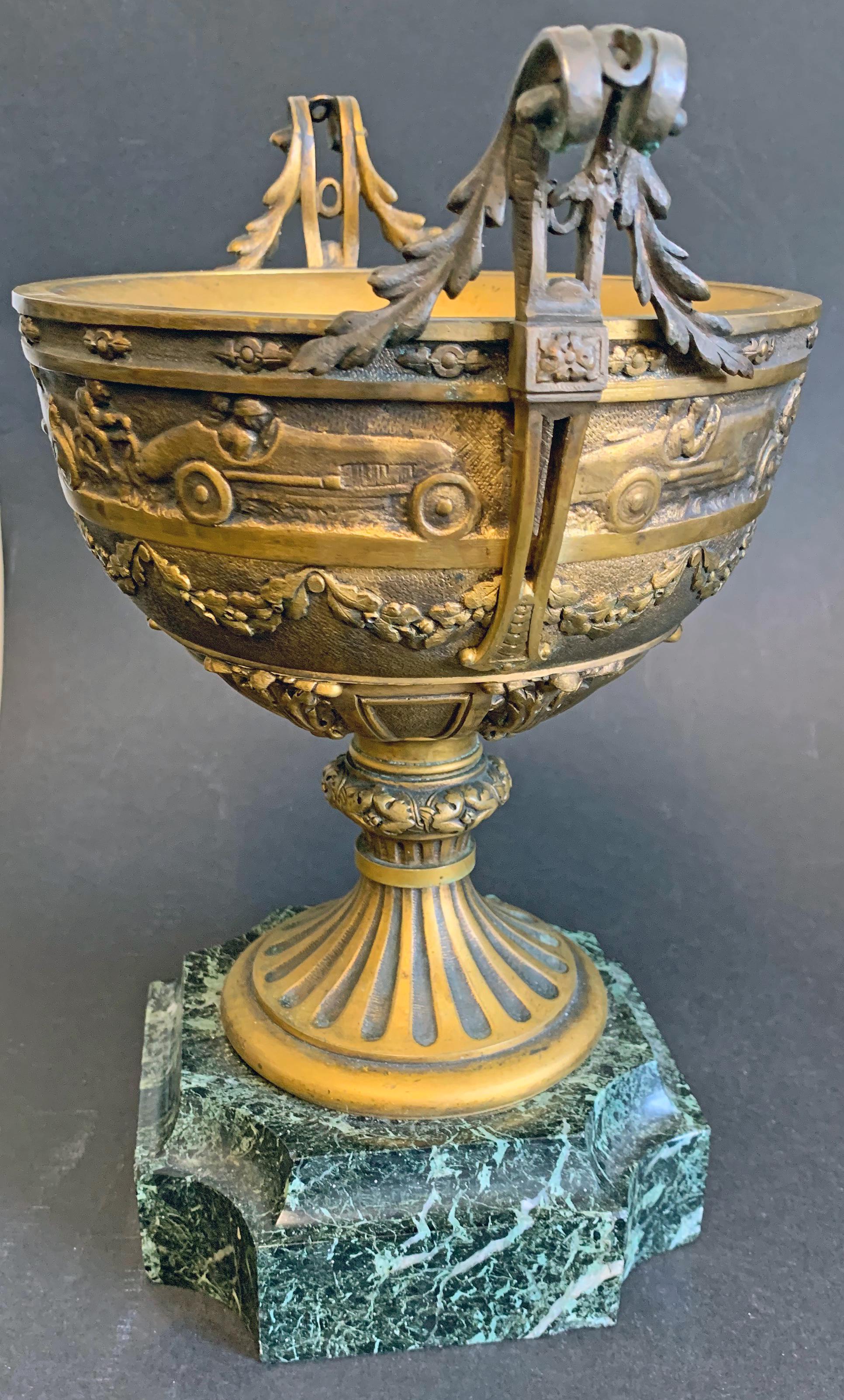 Rare, perhaps unique, this beautifully sculpted and cast bronze cup features a frieze of racing cars and motorcycles in the heat of the race, above a series of garlands with oaks leaves and acorns, foliate motifs and a fluted base. Signed 