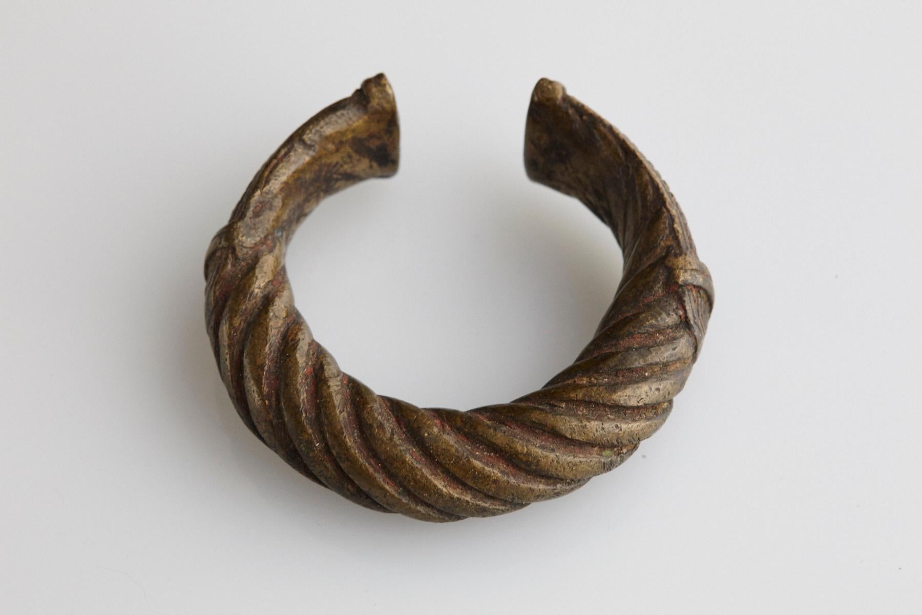 19th-century bronze currency bracelet / Manilla in horseshoe form with fixed opening. Intricate graphical swirled rope work design and tips are shaped with large flat ends with geometrical designs. This type of bracelet was used and worn by the
