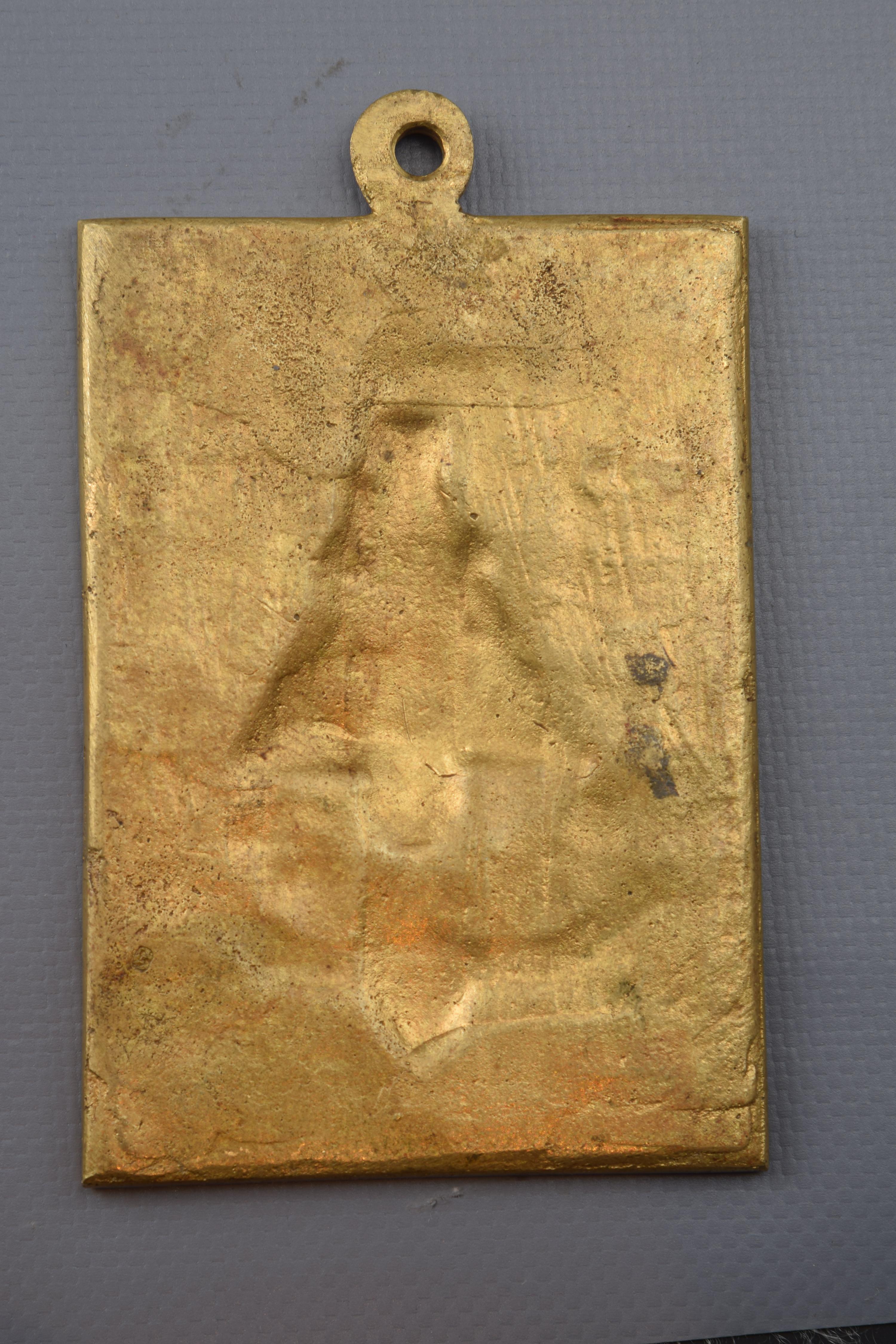 Devotional plaque, Our Lady of Covadonga. Bronze, 20th century.
Rectangular bronze plate that has a ring on the top and a simple frame to highlight the relief of the front. On a mountainous background in which a characteristic construction is