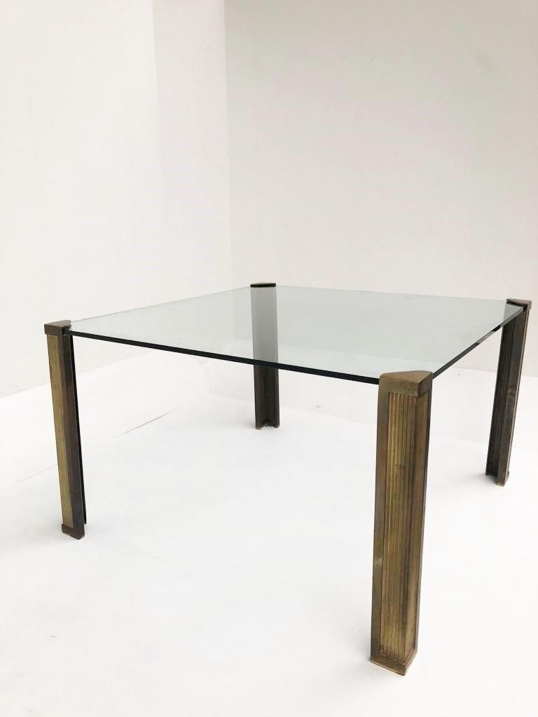 Impressive square glass dining table with cast bronze legs designed by Peter Ghyczy.

The thick glass top is supported in the corners by the heavy bronze legs so it looks to be floating.

Beautiful patina on the legs

Thick 15mm clear glass table