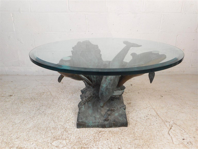 Very interesting modern coffee table. The base is made of bronze and features a representation of three dolphins playing atop a wave. Intricate details such as the dolphin's facial features and the wave's textured surface give this piece a life-like