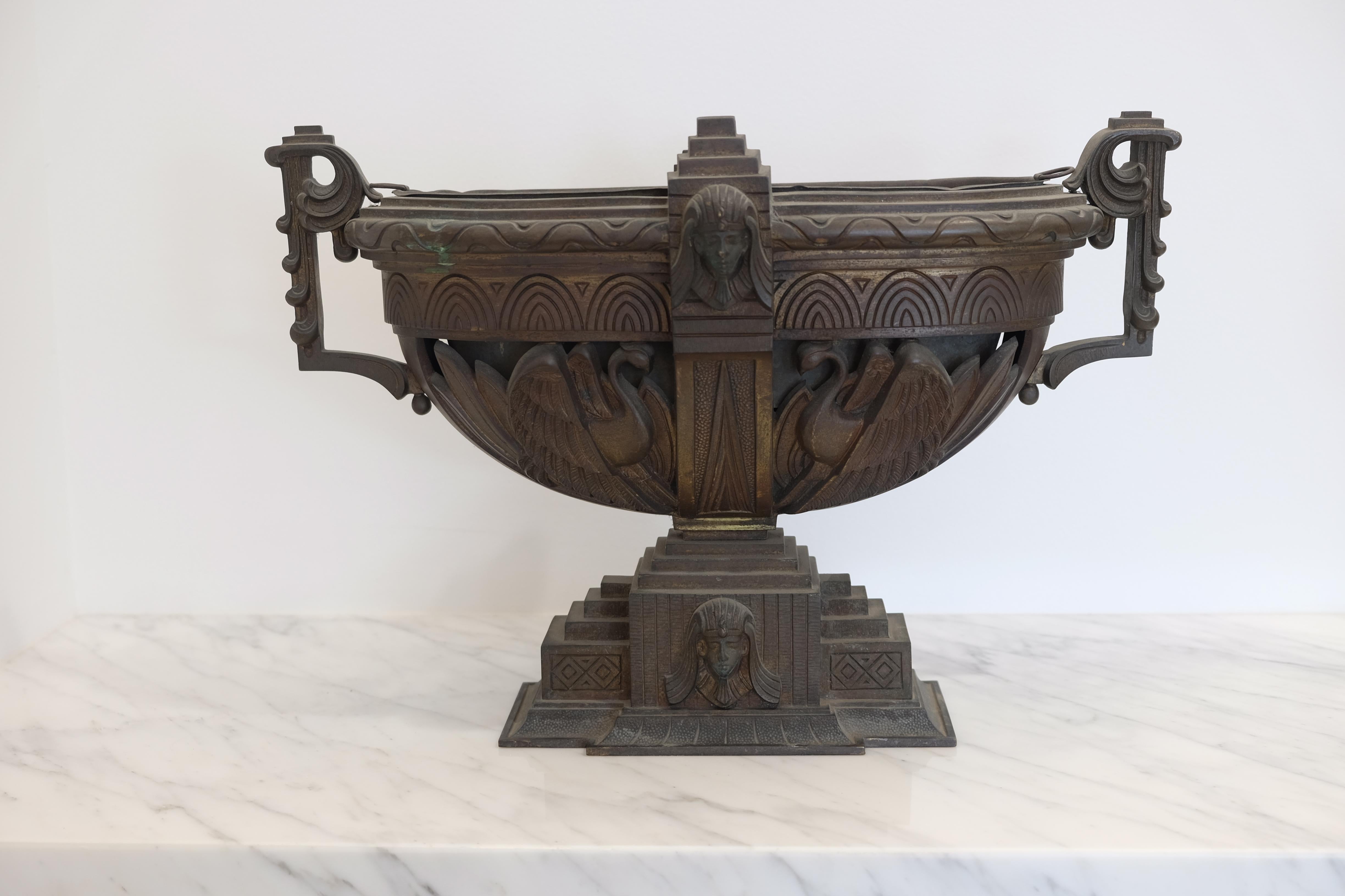 A bronze Egyptian revival urn having stylized handles and sphinx bust decorated border over swan decorated bowl.