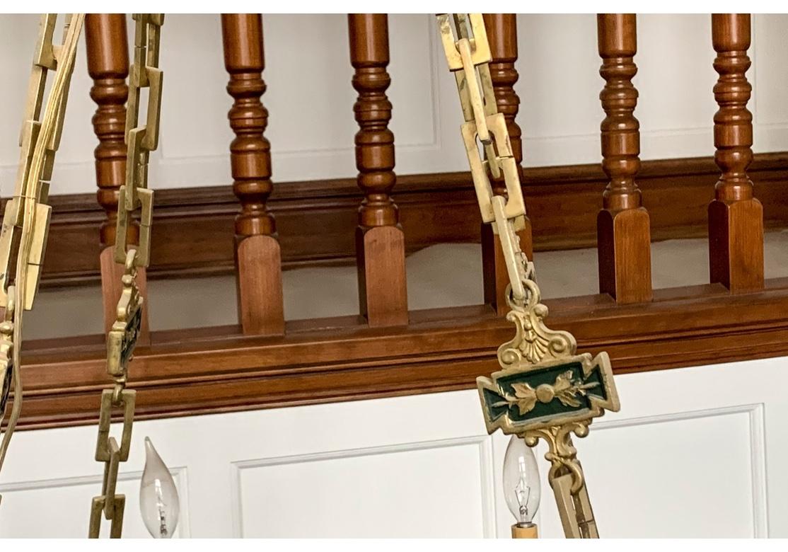 Impressive eight-light fixtures with wide frames in an elegant classical two-tone Gilt and Green Greek key motif. With applied oval and round bronze rosettes underneath the frames. The lights with urn form sockets alternate with raised bud and