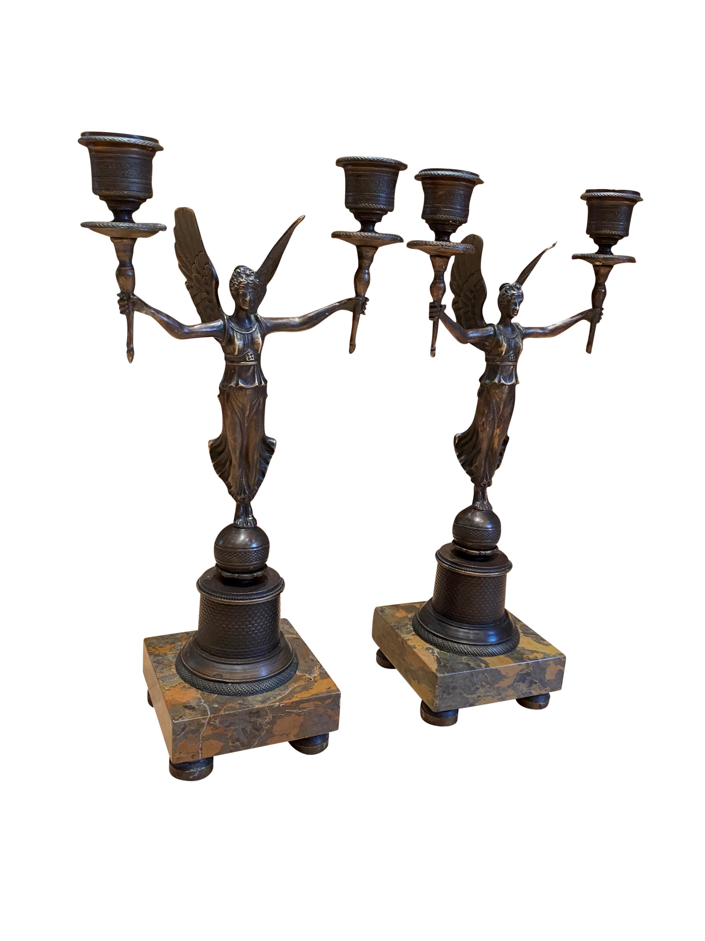 A stunning pair of French bronze Empire style candelabras. Perfect left and right, each maiden holds aloft the two ormolu candle branches. The pair Stand on a globe ball with pattern frieze on a beautiful two-tone marble.