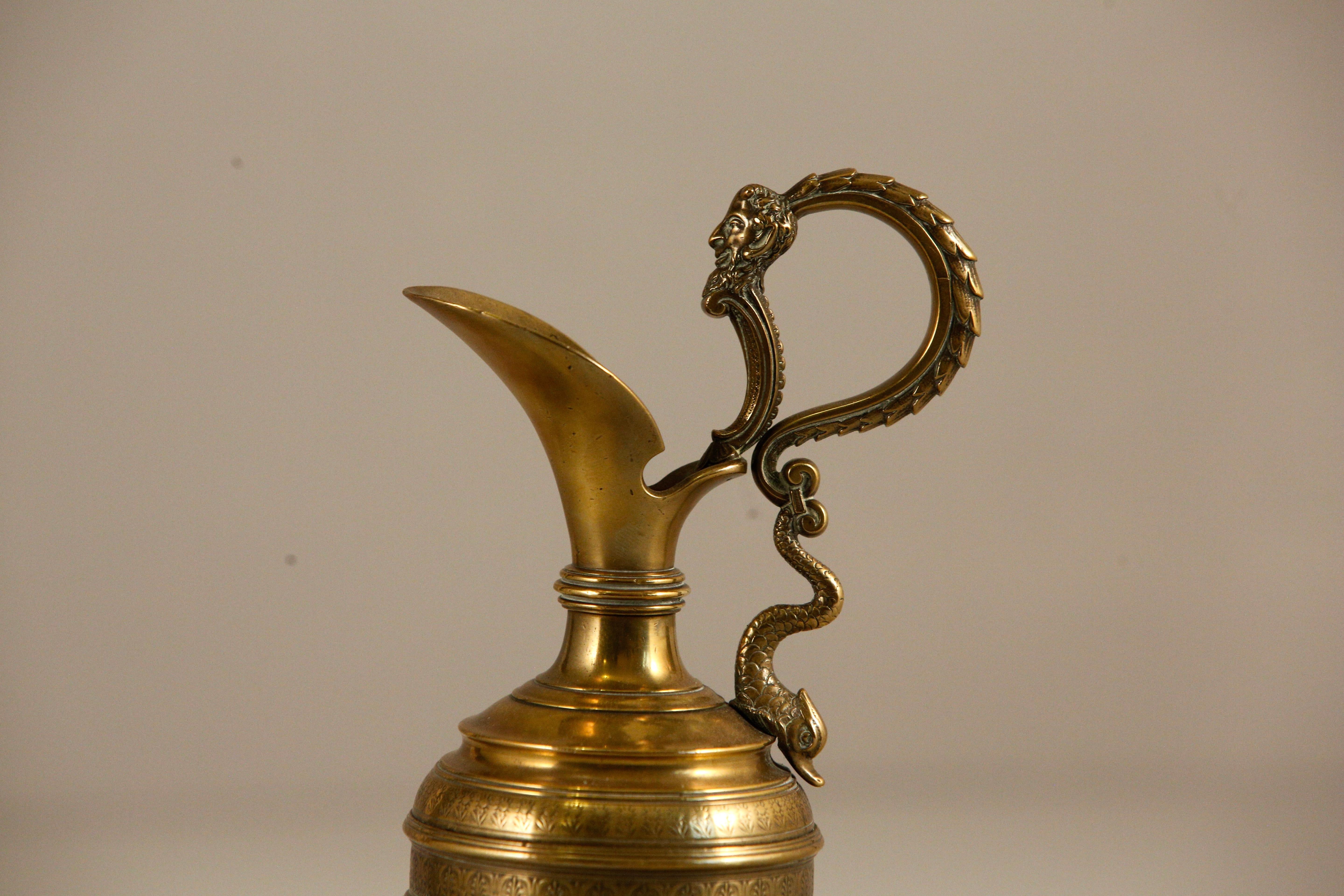 Small bronze ewer with Bacchus and dolphin figural handle, engraved solid oval centerpiece mounted on a circular base. 