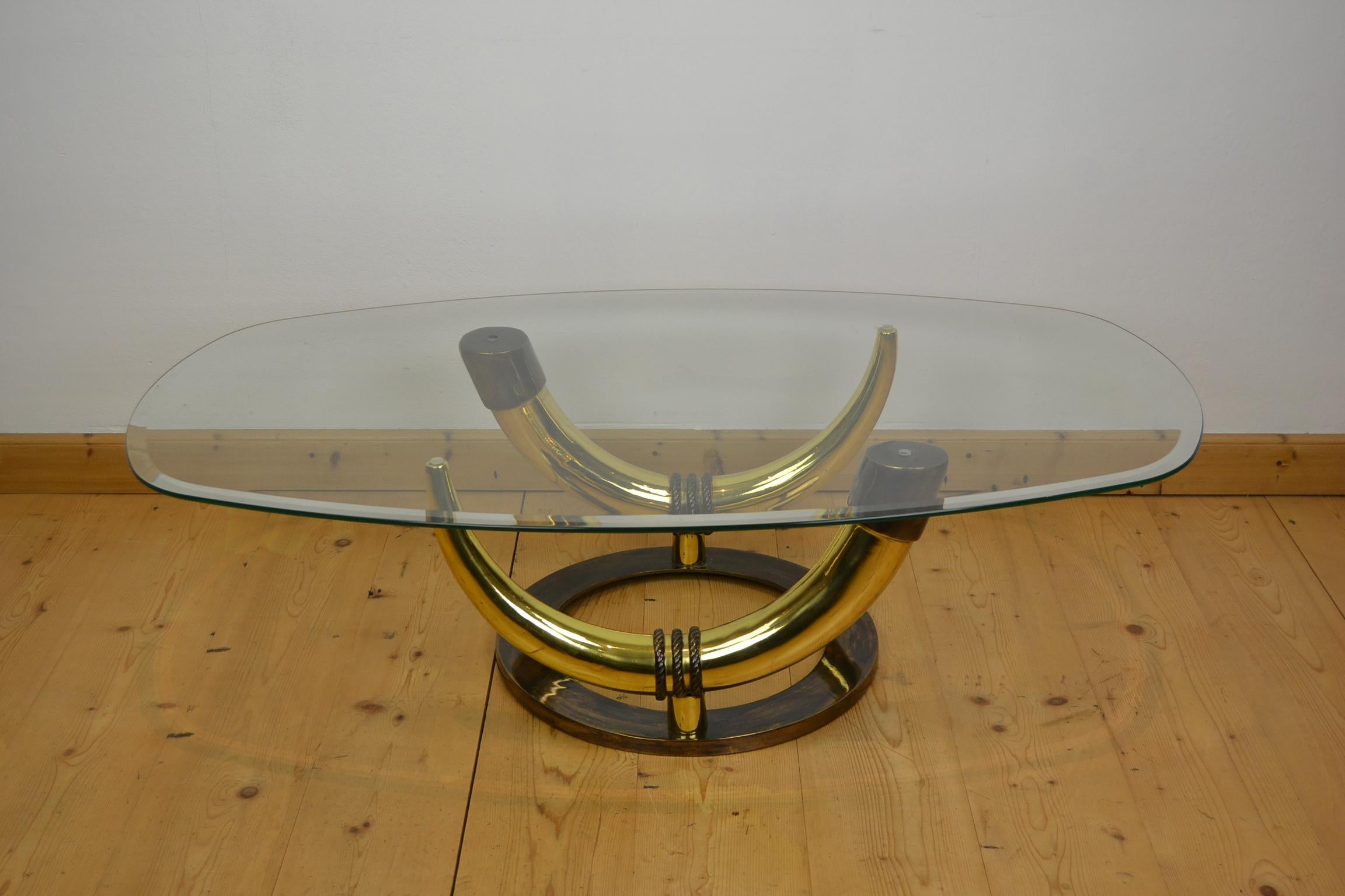 Bronze tusk coffee table. 
This great looking faux elephant tusk table is made of bronze, 
has 2 tusks and an oval beveled glass top. 
The faux elephant teeth have a beautiful golden color. 
It's a great table to place in your interior or