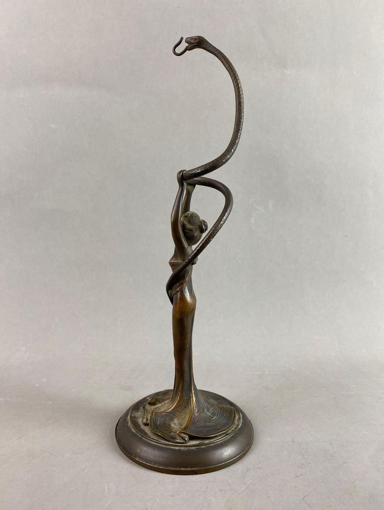 Bronze statue of a young woman in a strapless dress with a billowing bottom, holding a large snake. At one time the piece was d’or bronze, although most of the gold leafing has rubbed off. In the style of Franz Bergman. Unsigned. 