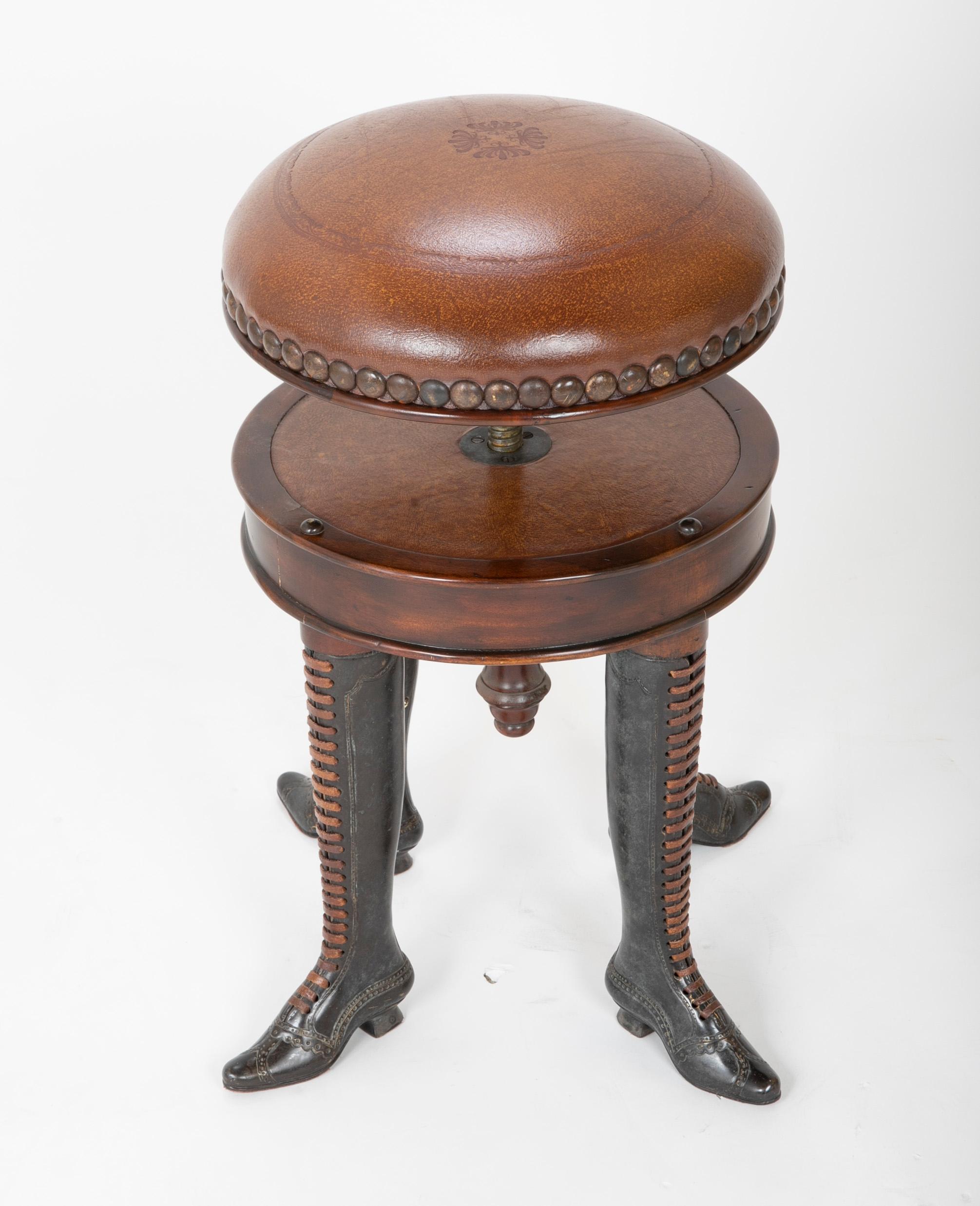 An adjustable, revolving stool having four bronze legs and feet in the shape of boots with leather upholstered brass studded seat.