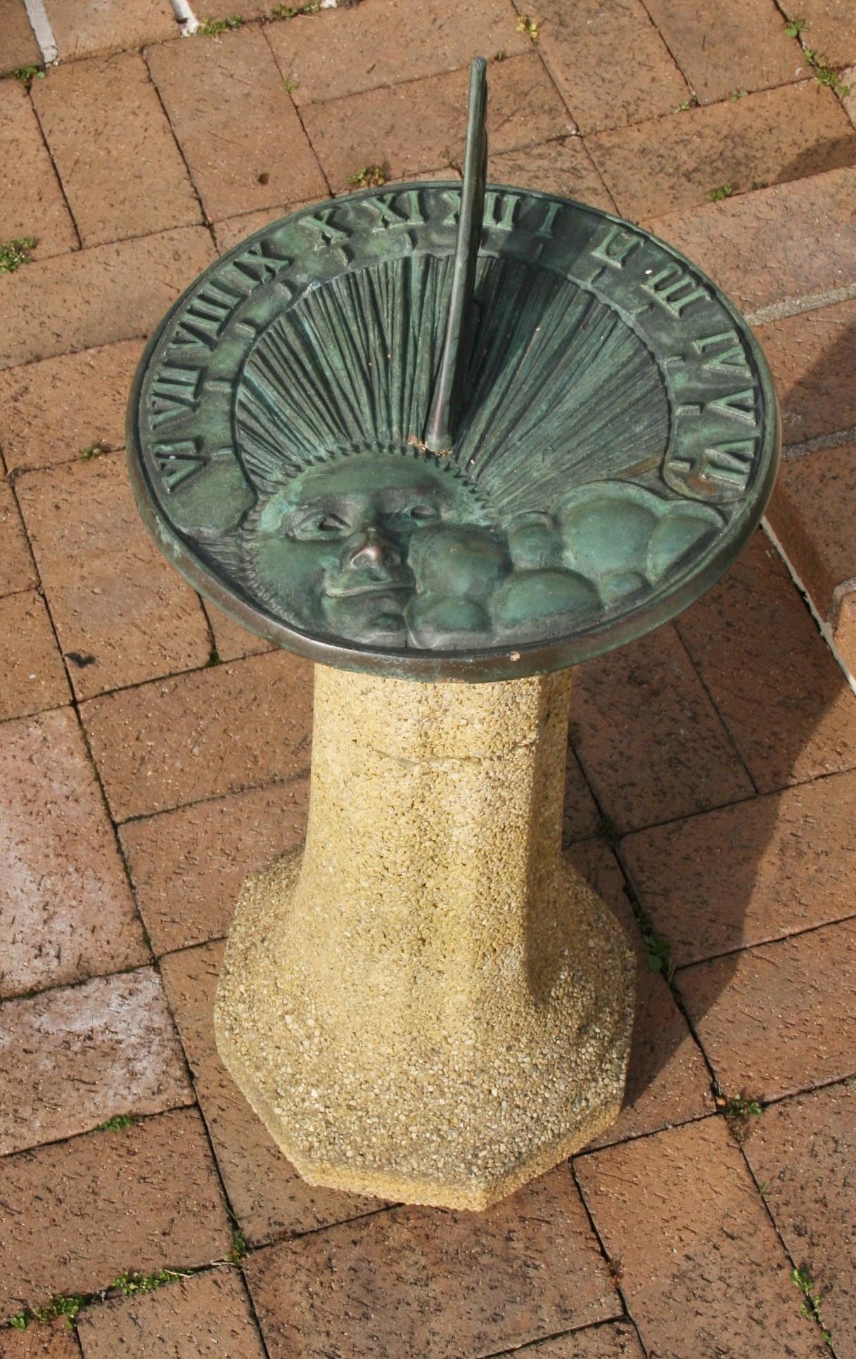 3-478 bronze sundial and pebble base with decorative sun on surface.